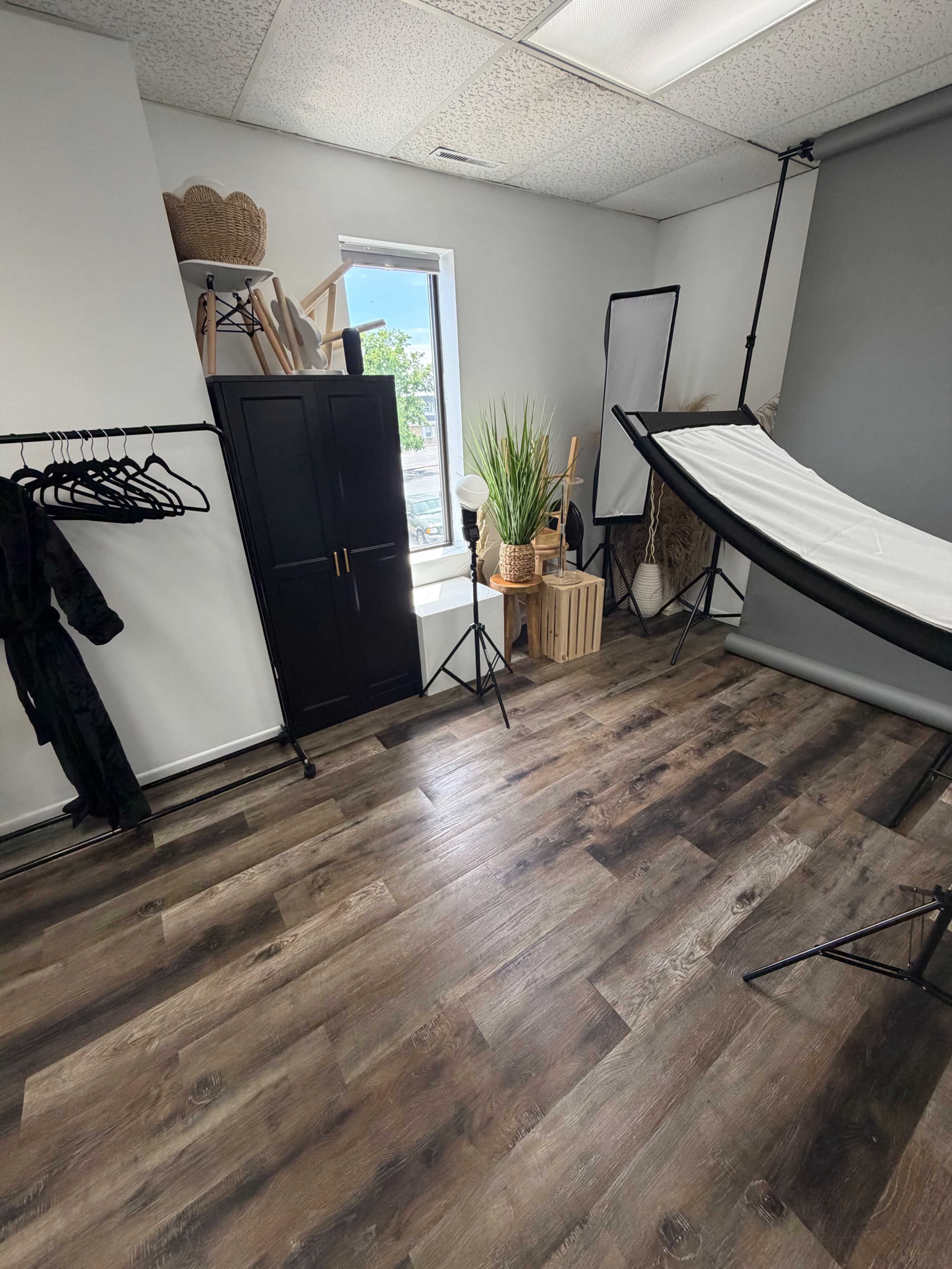 The image shows a bright, organized studio space with a clothing rack, a black cabinet, and a photography backdrop setup.