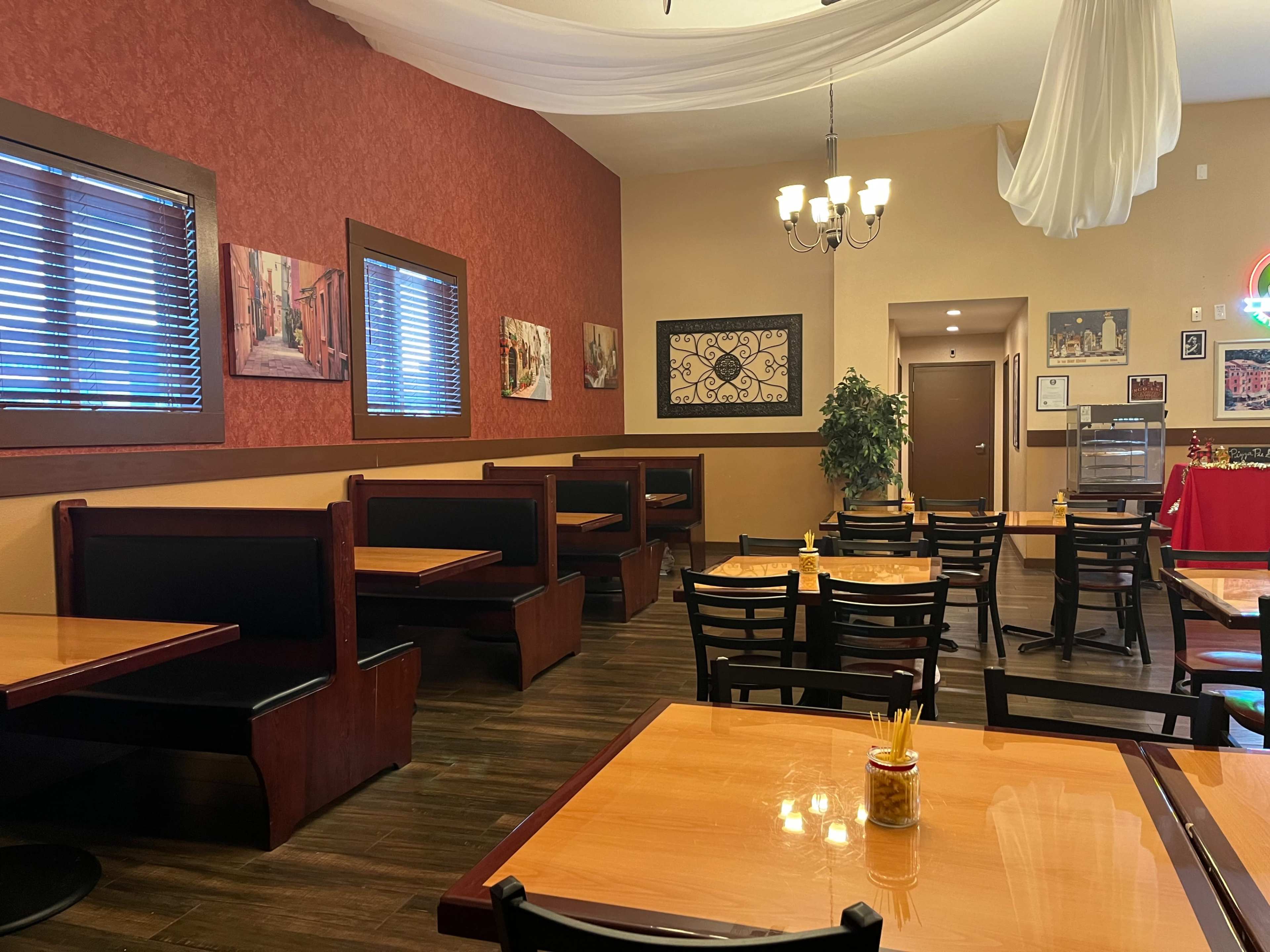 A semi-filled restaurant interior with wooden tables, black chairs, and booth seating, featuring decorative wall art and soft lighting.