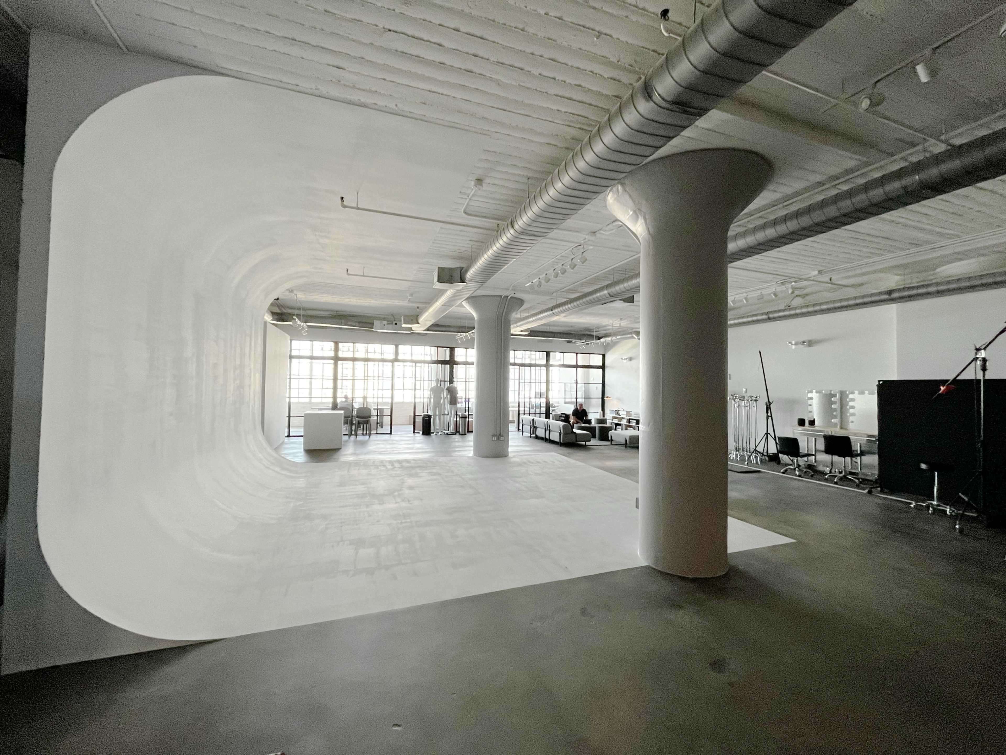 A spacious studio with a white, curved backdrop, large windows letting in natural light, and minimal furnishings.