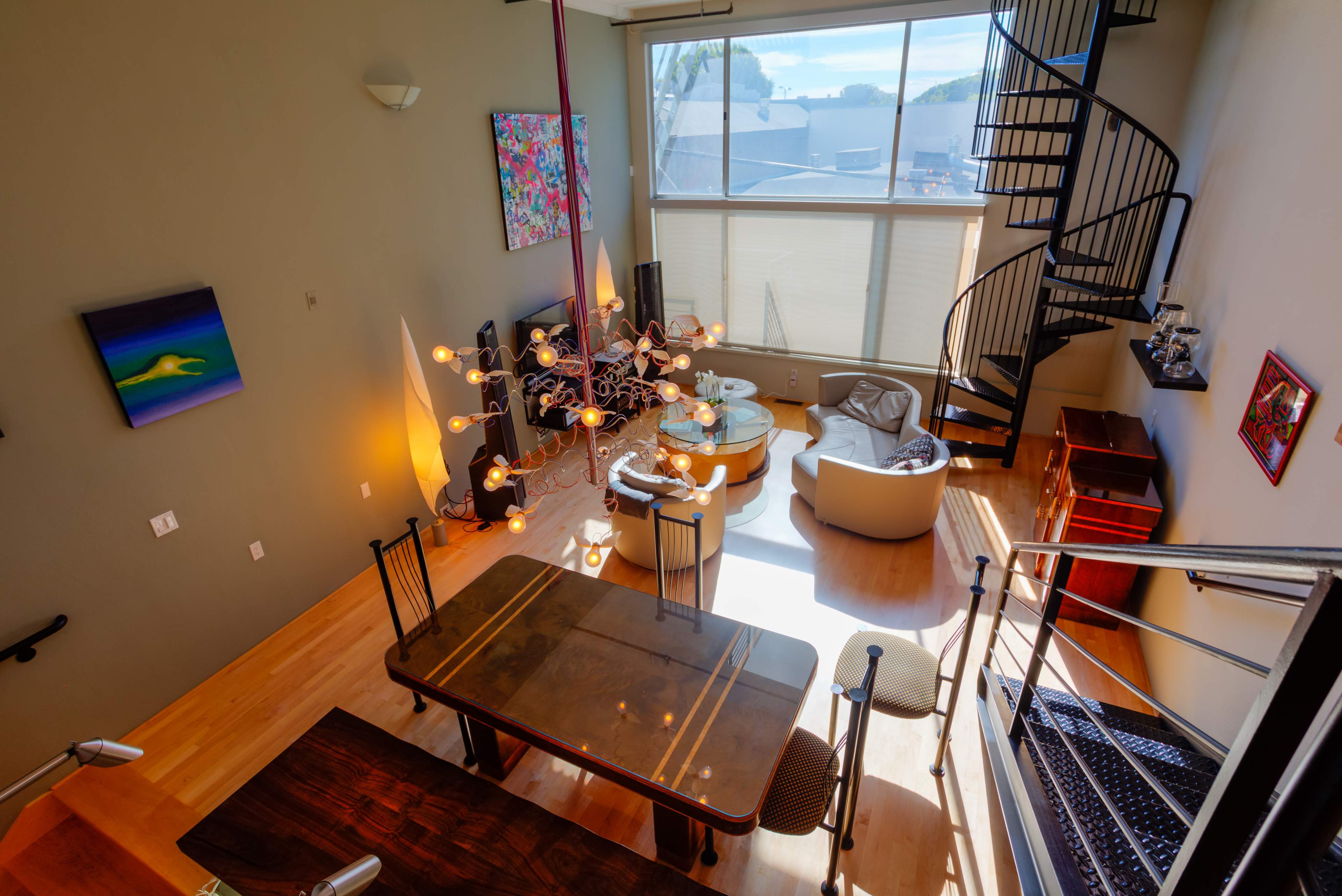 A modern, multi-level living space features a dining area with a wooden table, a lounge with a circular sofa, and a spiral staircase leading to a loft.