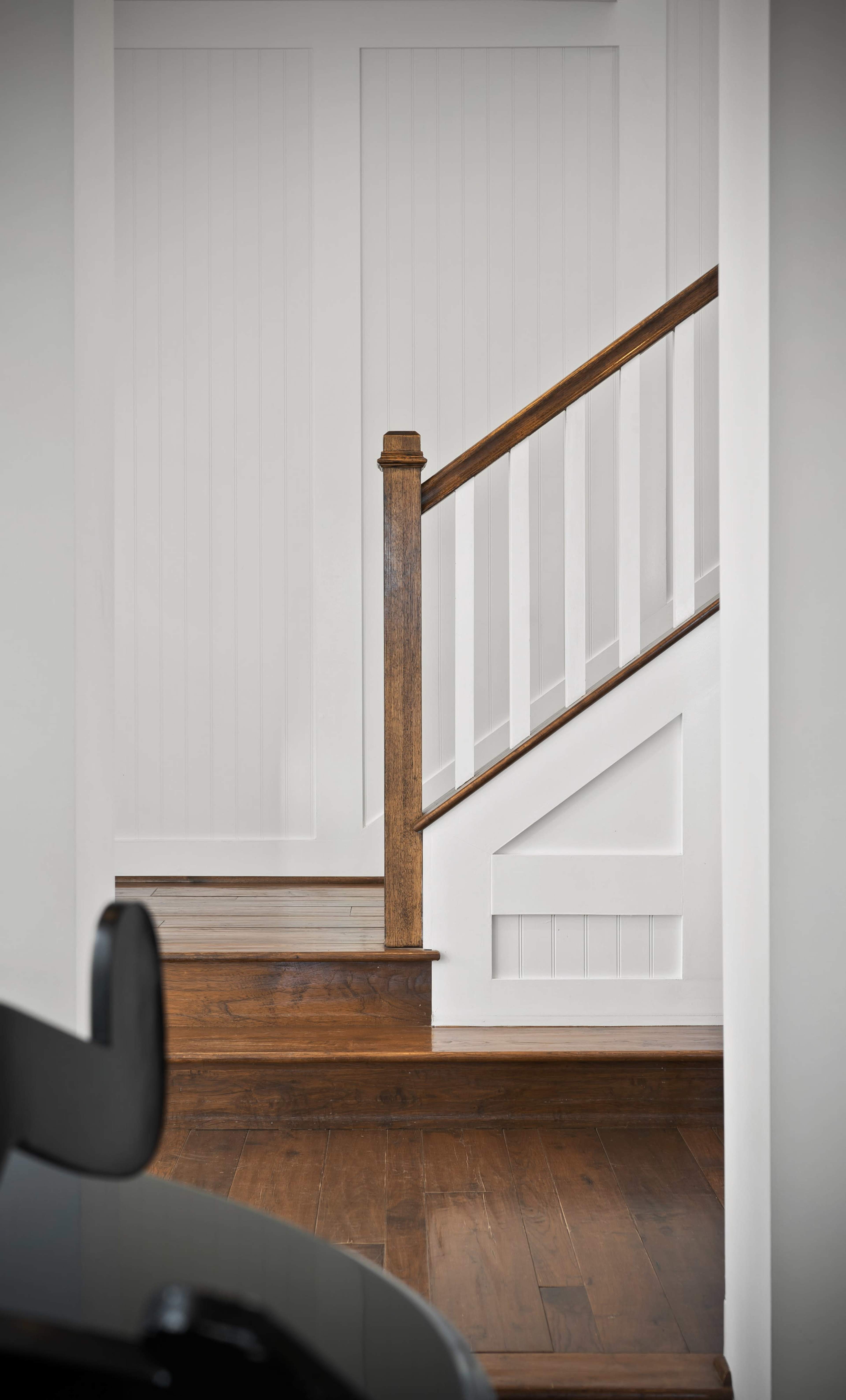 A wooden staircase with a handrail and white balusters leads to an upper level in a light-colored hallway.