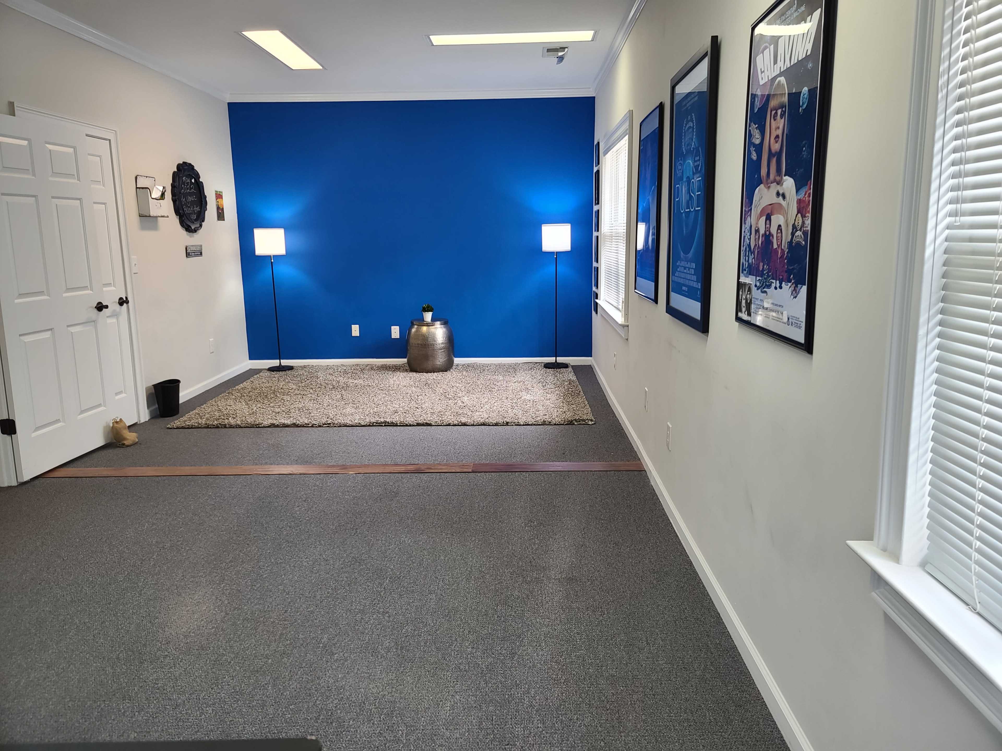 A room with a blue accent wall, two lamps on either side, a gray rug on the floor, and framed posters on the walls.
