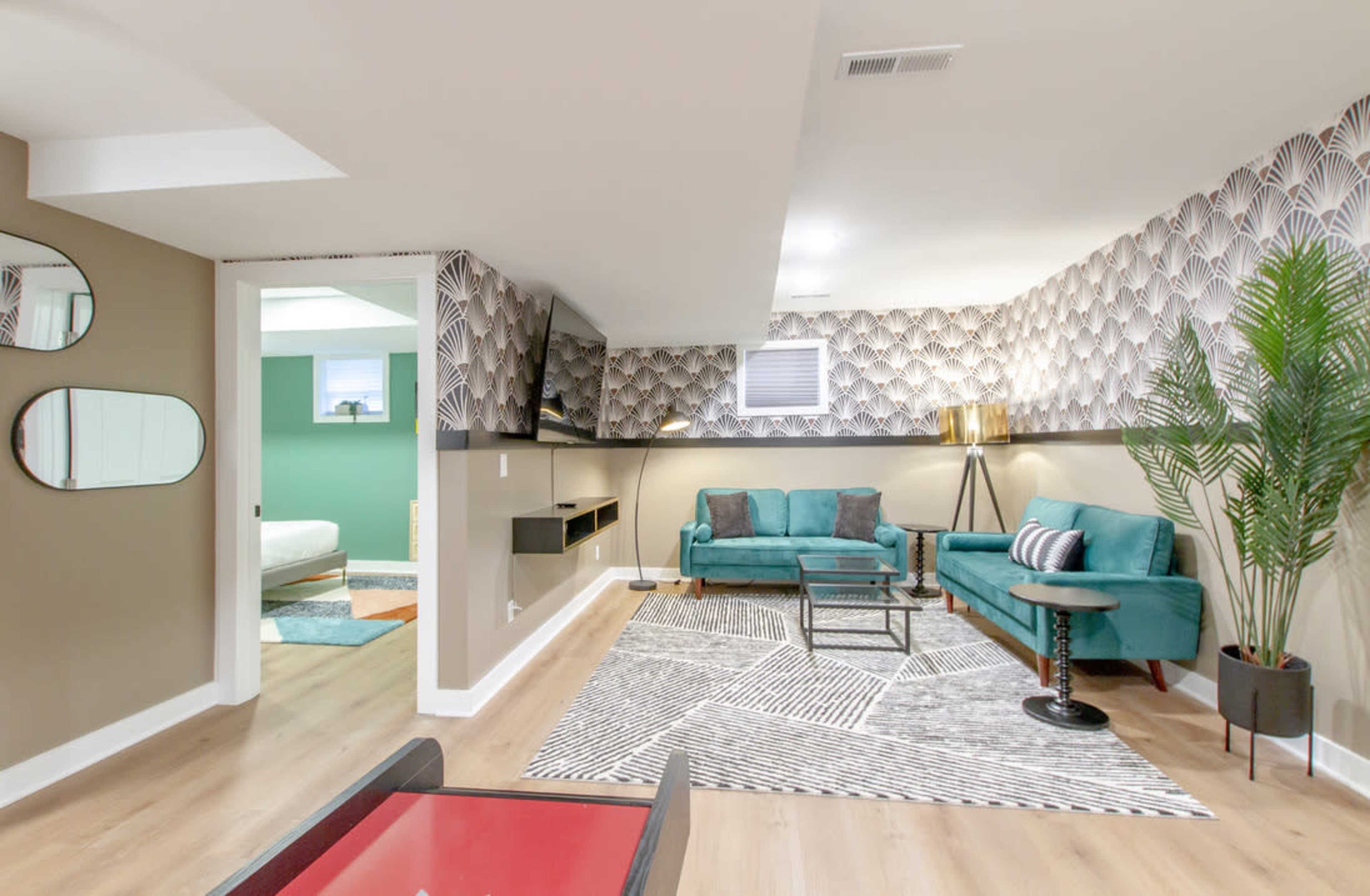 The image shows a modern living space featuring teal couches, a patterned wall, a television mounted on the wall, and a geometric area rug.