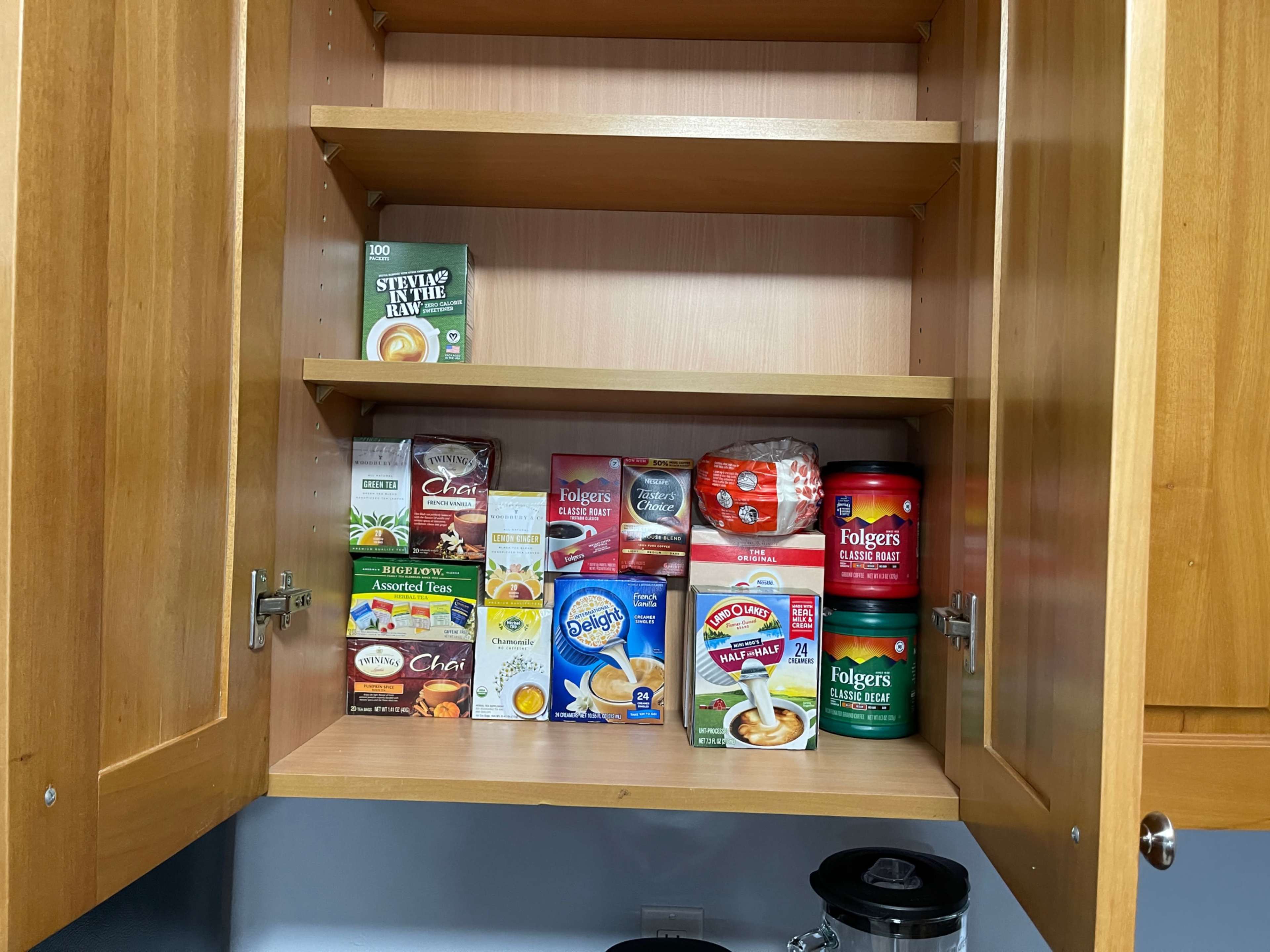 A kitchen cabinet shelf filled with various boxes and containers of tea, coffee, and sweeteners.