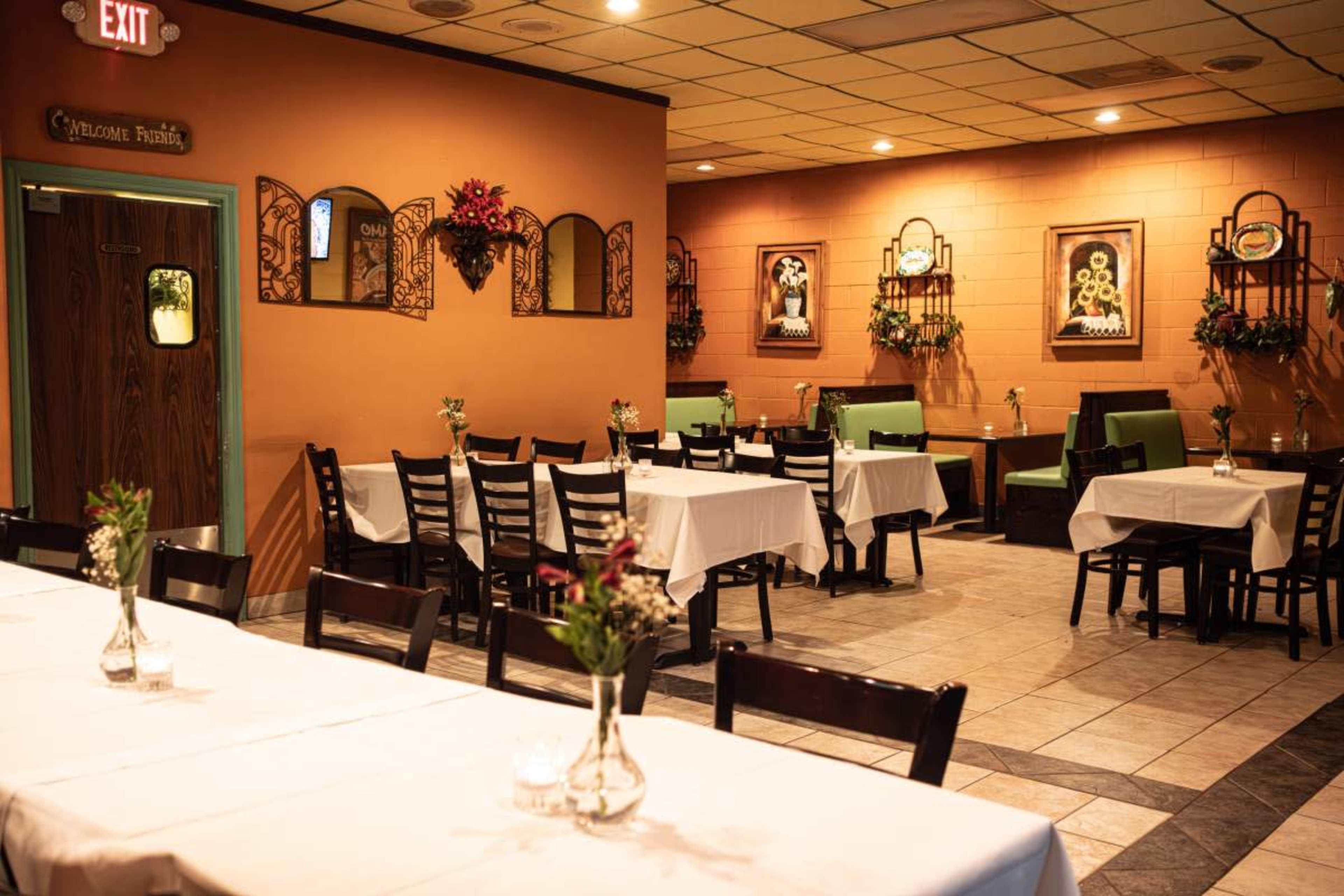 The image shows an interior of a restaurant featuring tables with white tablecloths, decorative plants on the walls, and green seating along one side.