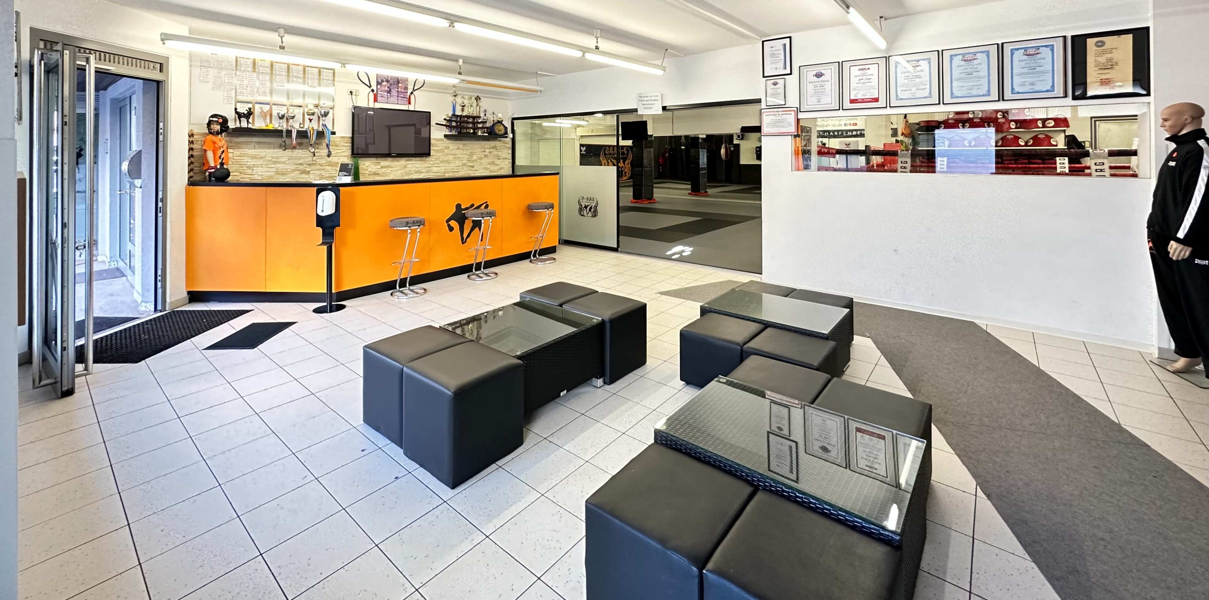 The image shows a gym reception area with seating, a counter, and training facilities visible in the background.