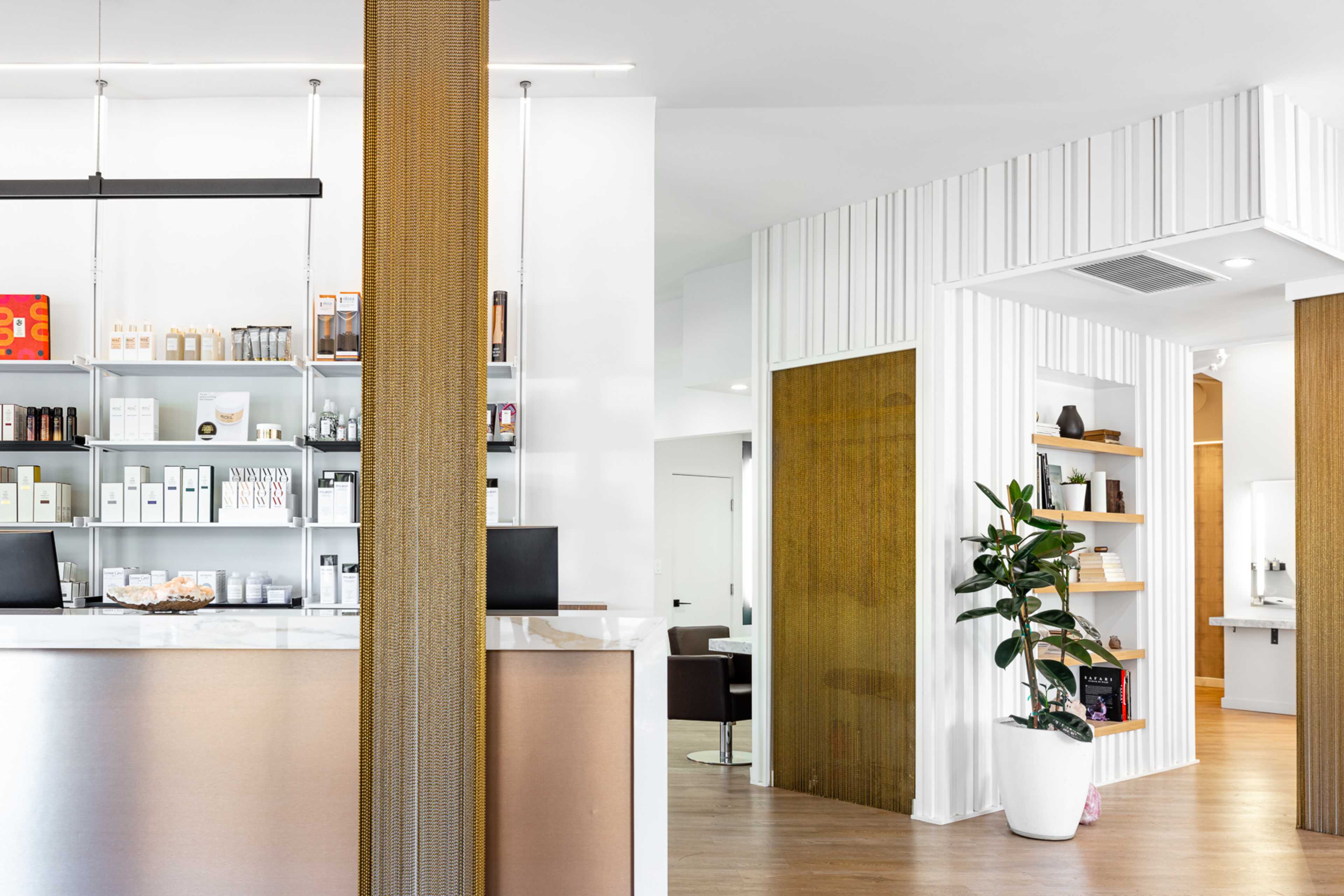 A modern reception area with a sleek counter, organized shelves displaying products, and a green plant in a white pot.