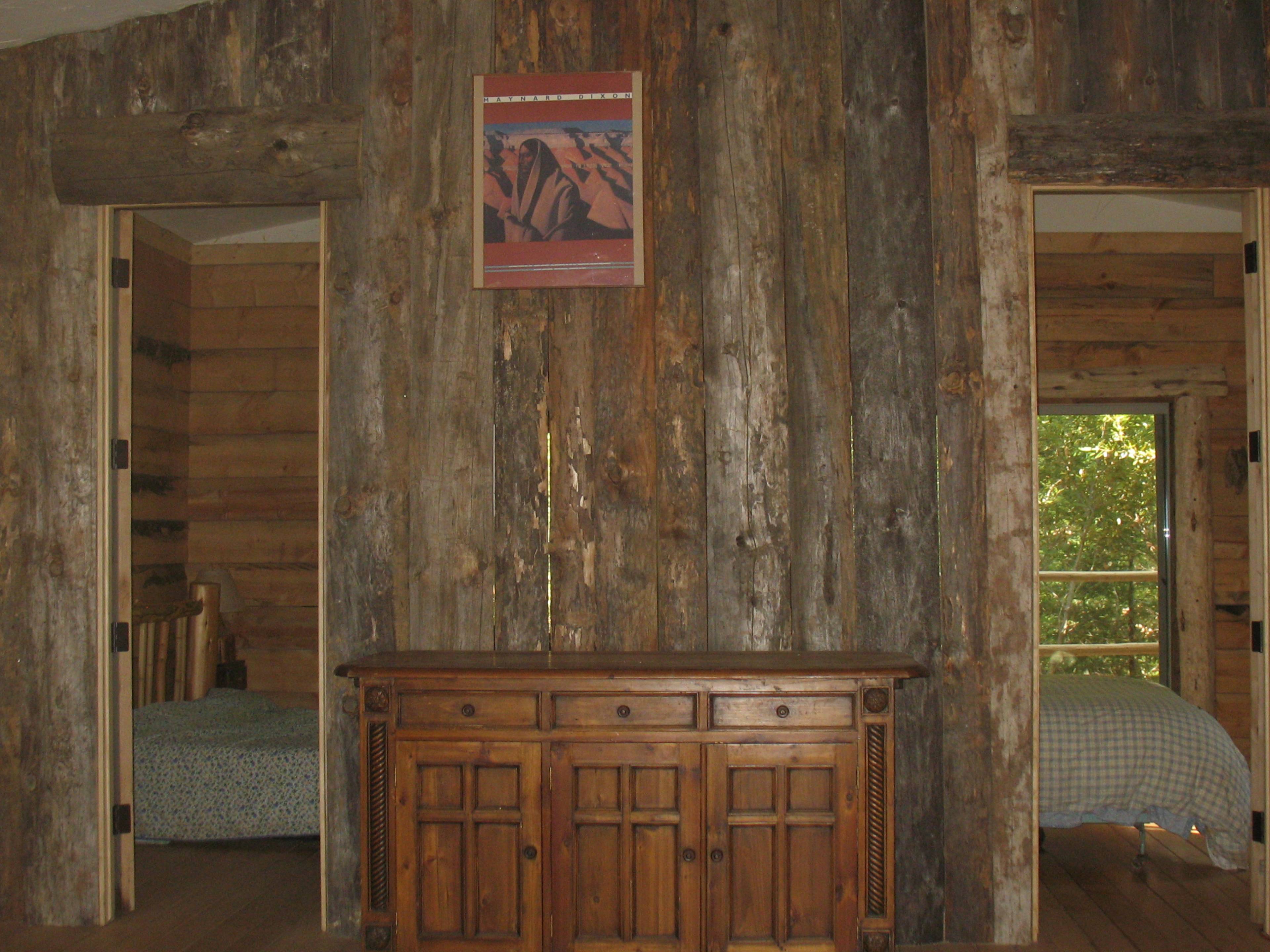 A rustic interior with wooden walls, a wooden cabinet in the center, and two doorways leading to separate rooms.