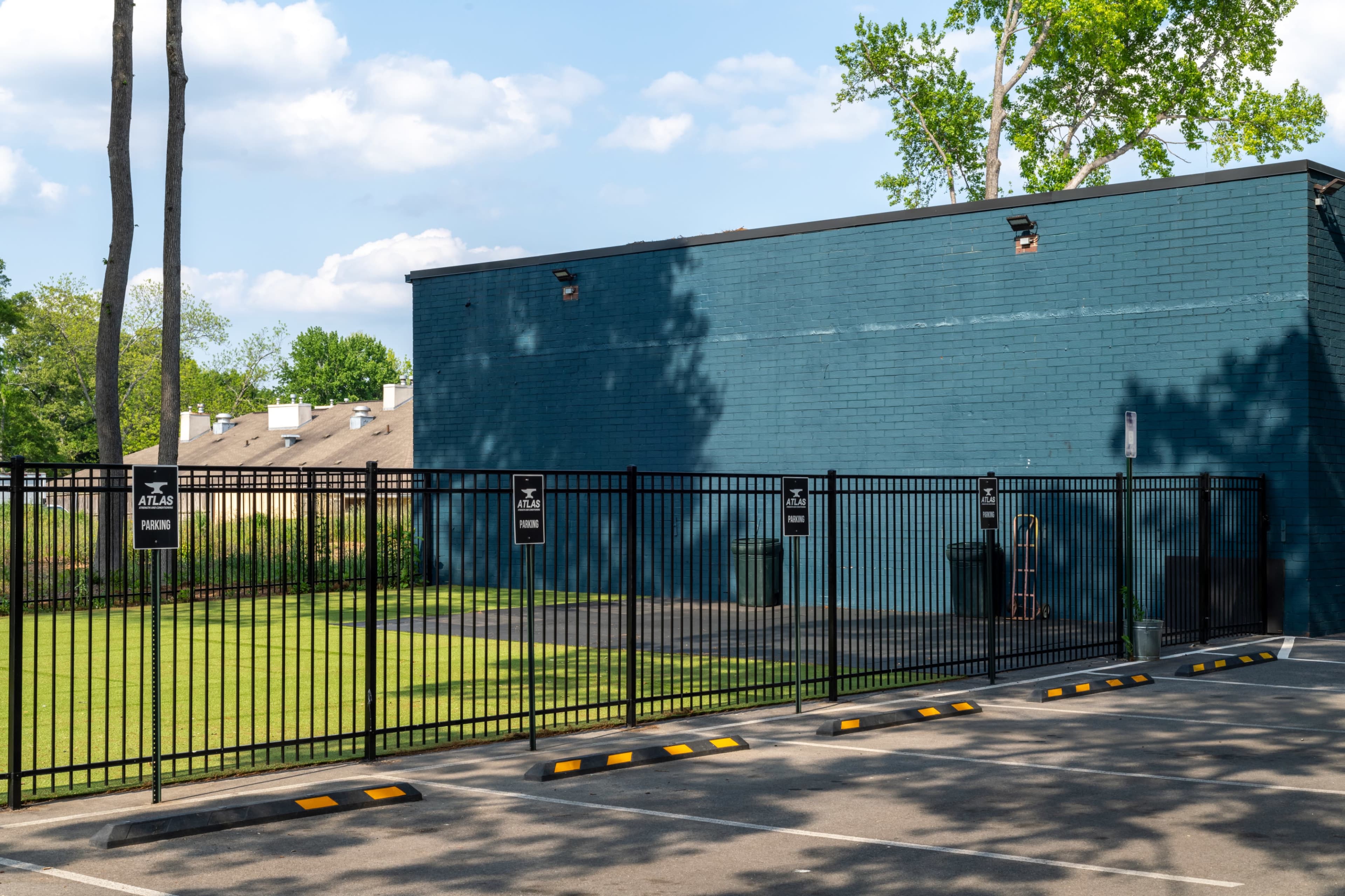 A blue brick building with a fenced-in area and parking spaces is visible under a partly cloudy sky.