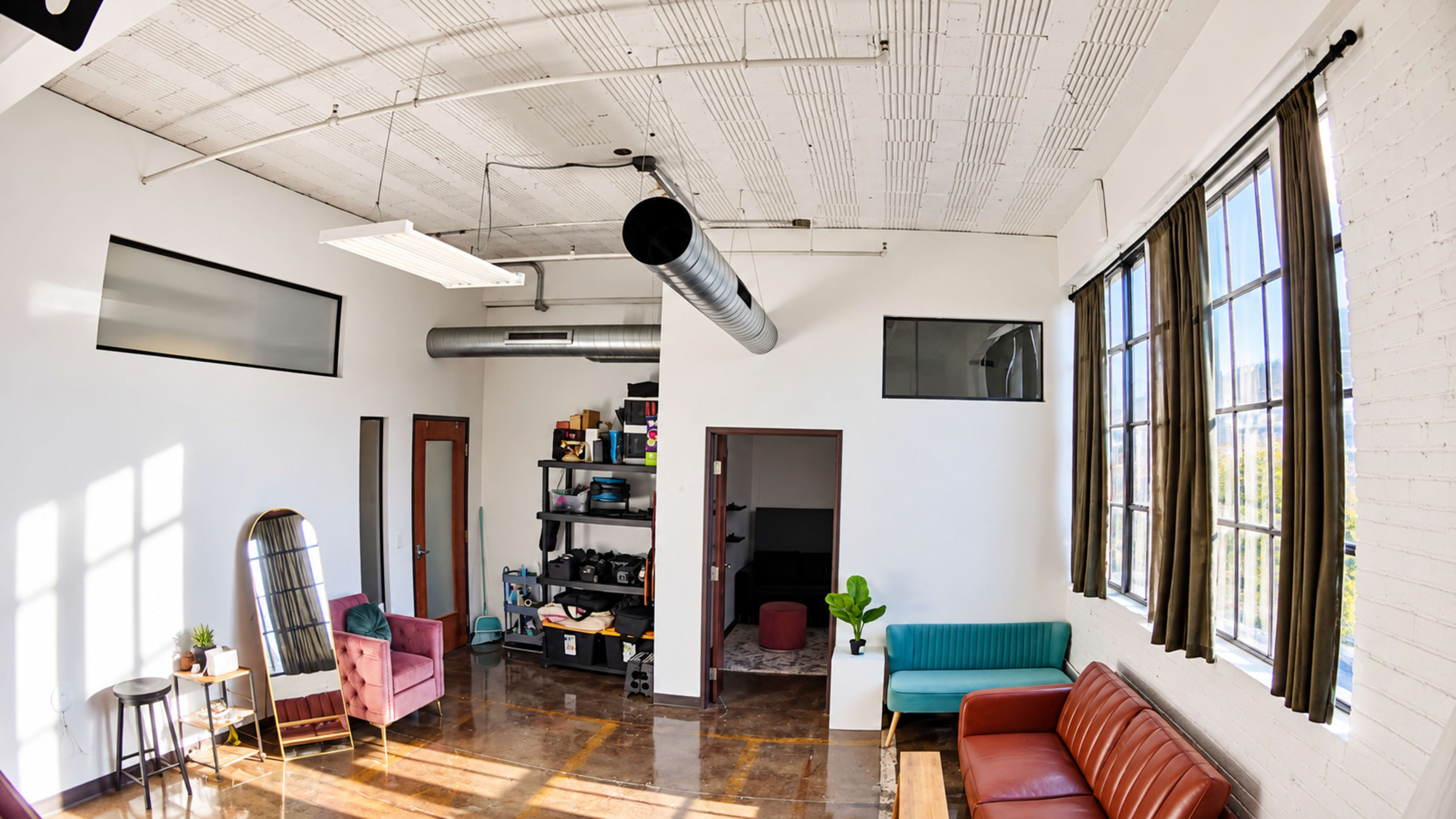 The image shows a modern, open-concept room with large windows, a mix of seating areas, and industrial-style elements.