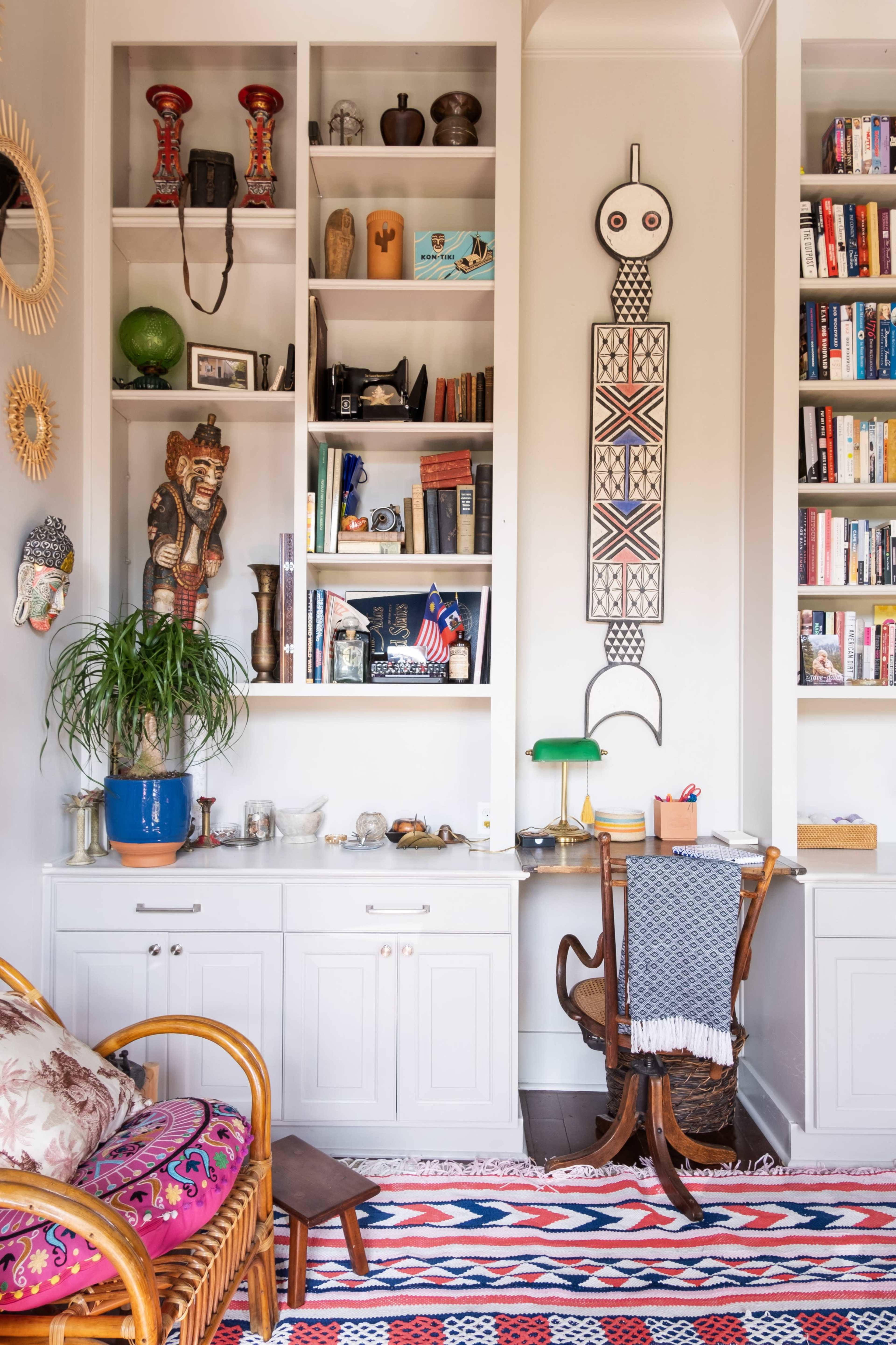 The image shows a cozy living room corner featuring a bookshelf filled with decorative items and books, a wooden chair, and a patterned rug.