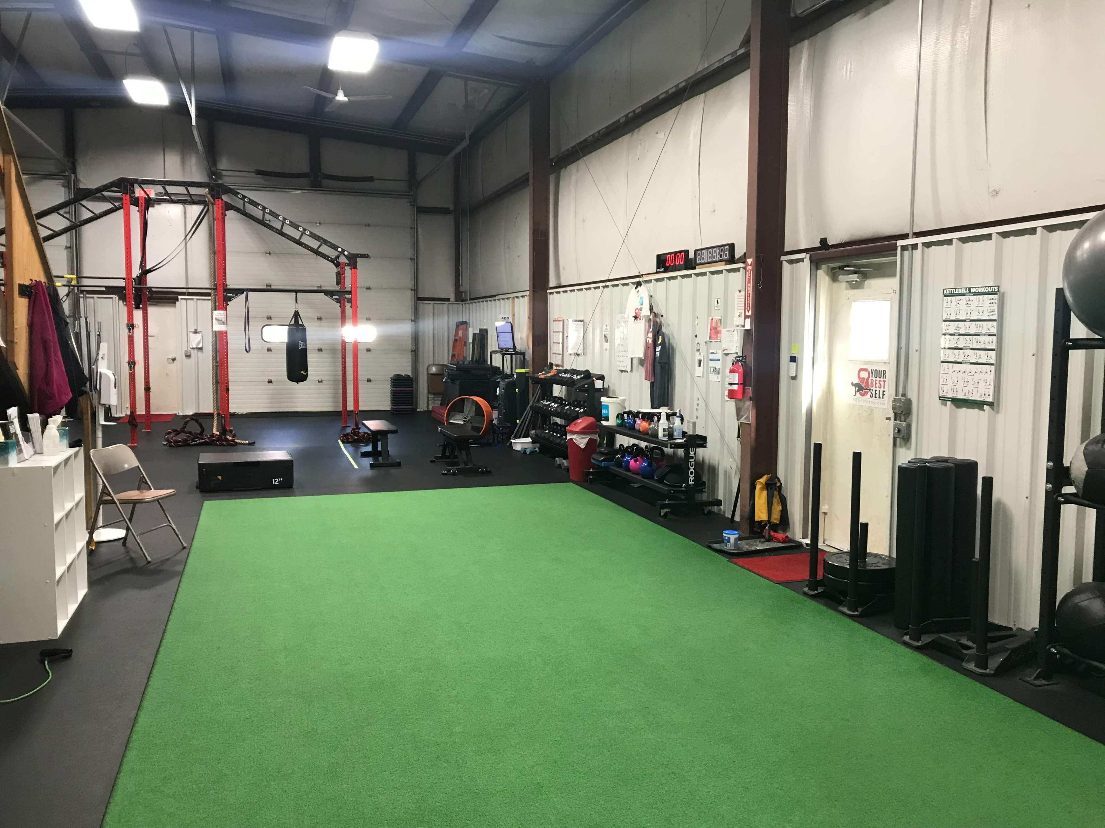 A gym interior with green turf flooring, exercise equipment, and a boxing bag suspended from a frame.