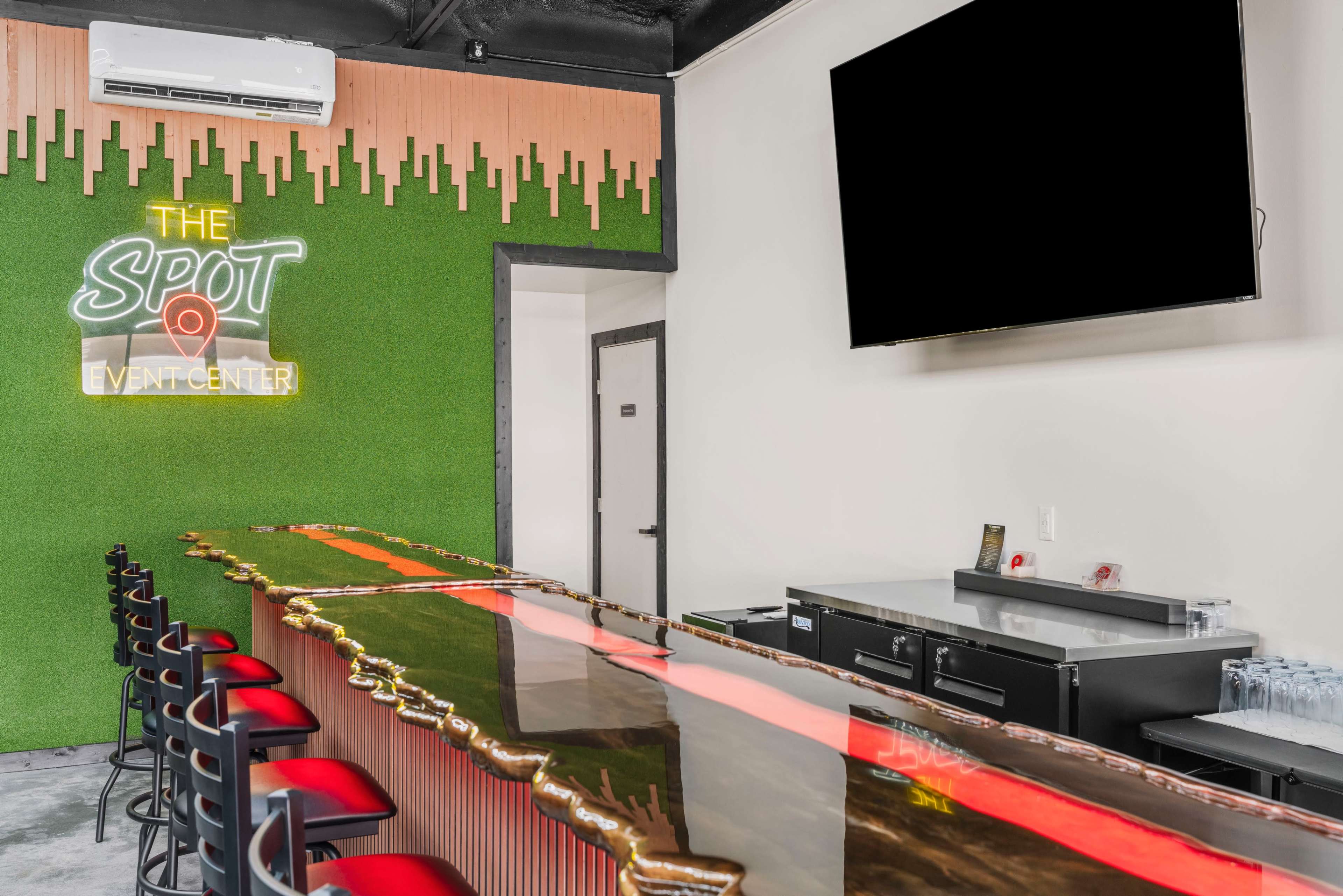 The image features a modern bar area within an event center, highlighted by a green wall with "The Spot" sign, a sleek countertop, and high stools.