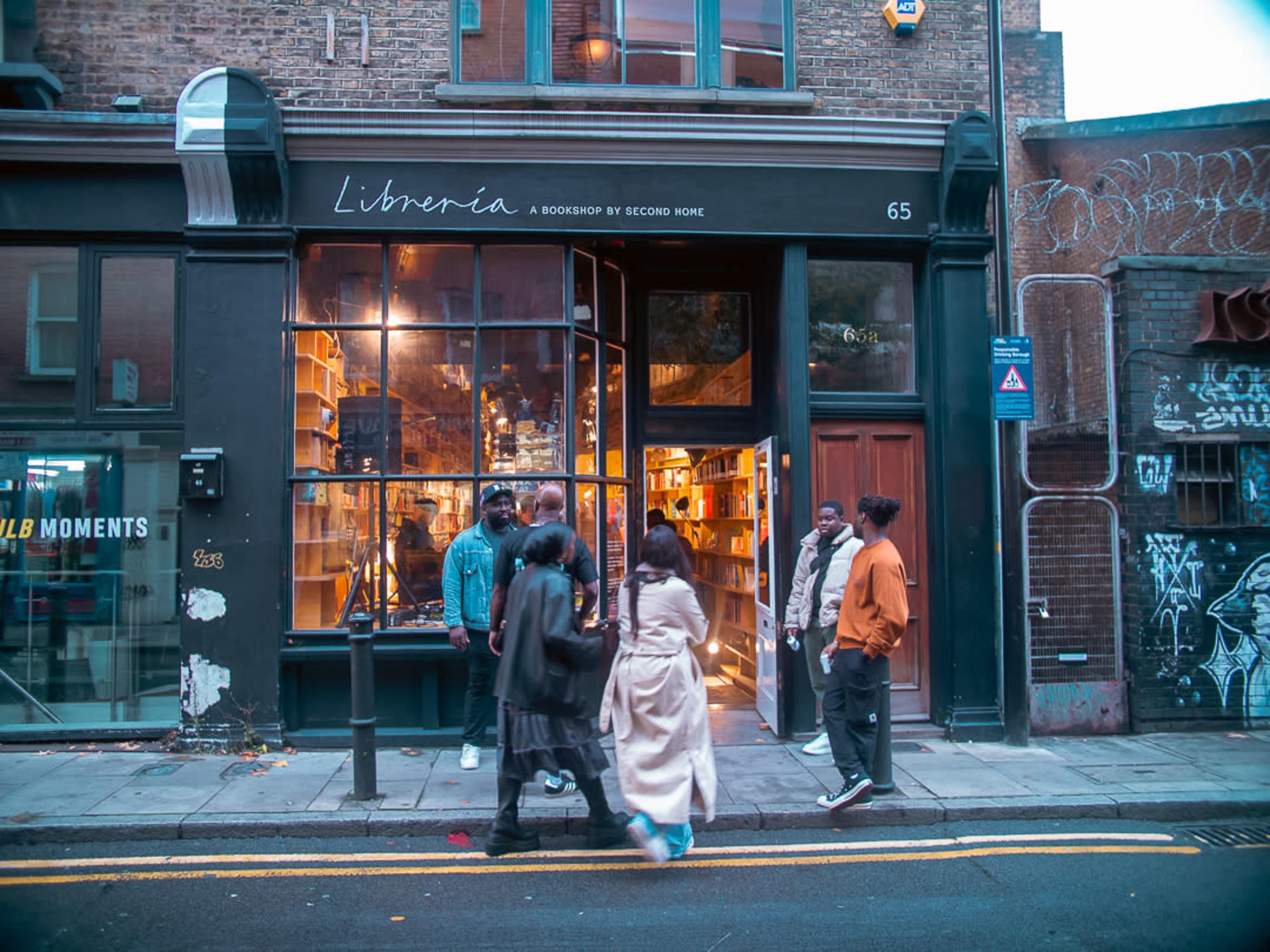 A group of people stands outside a cozy bookstore named "Librenia," which features large windows showcasing shelves filled with books.
