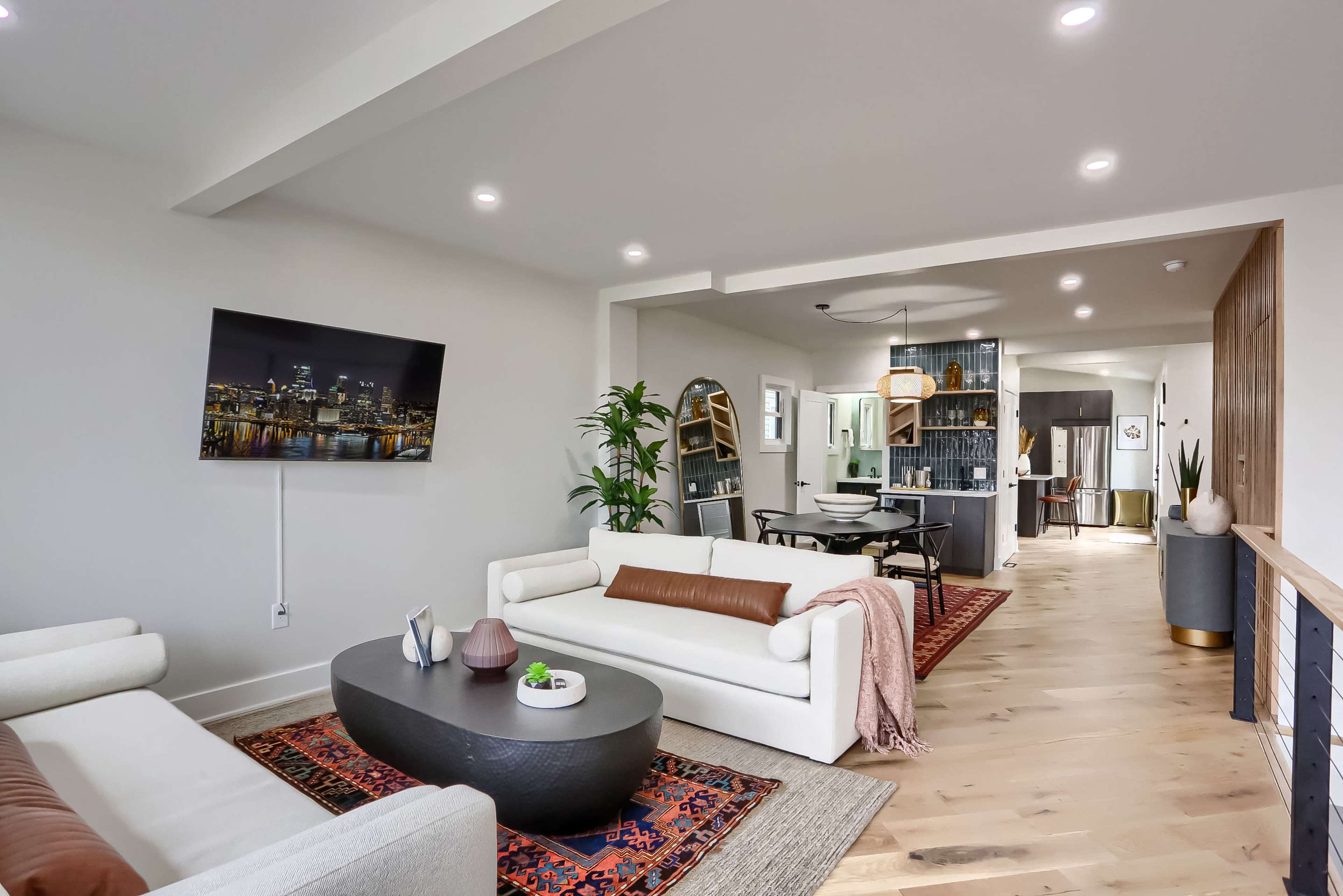 A modern living space featuring a white sectional sofa, a dark coffee table, and an open layout leading to a dining area and kitchen.