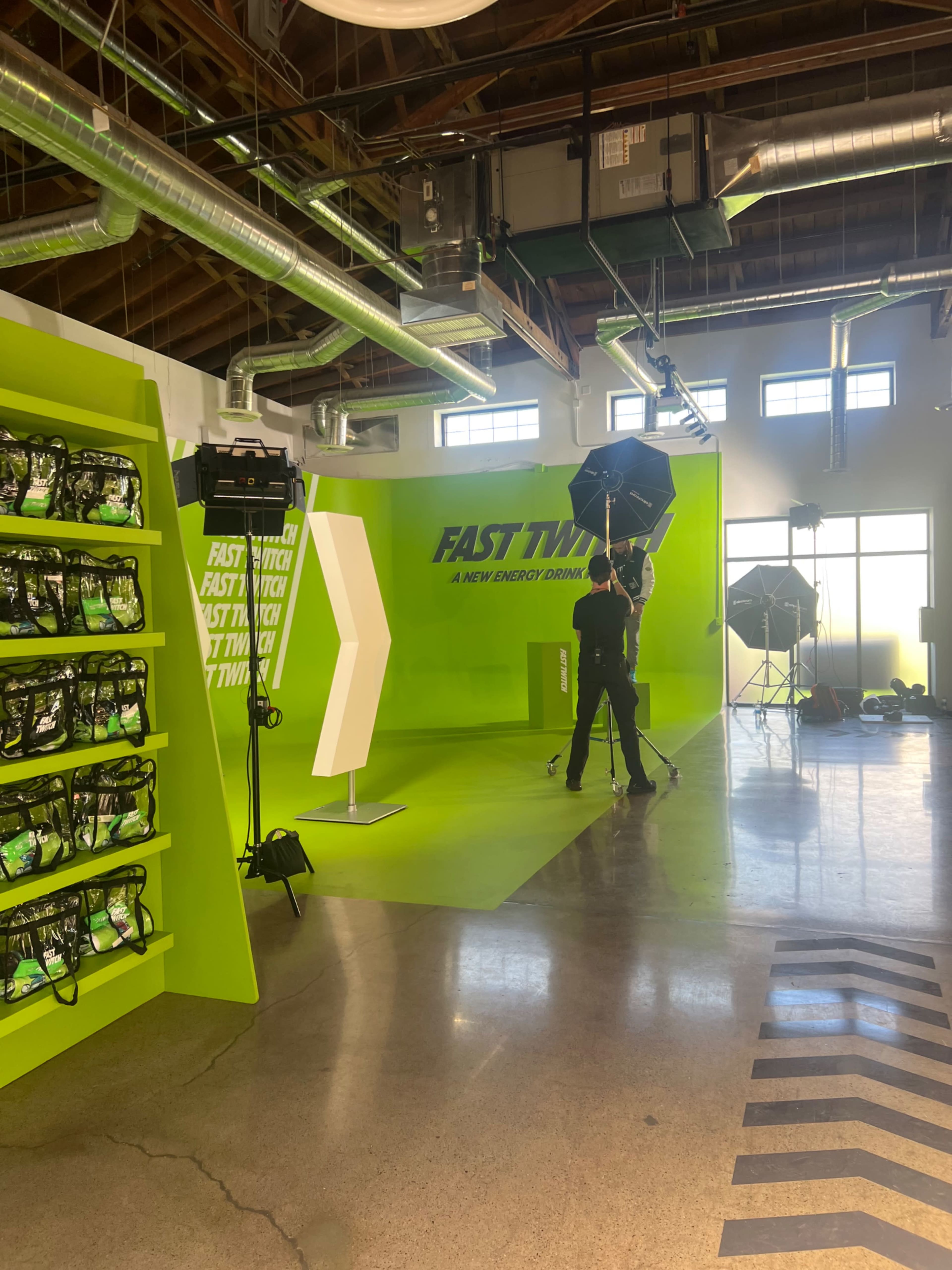 A person is setting up lighting equipment in a brightly colored studio space featuring a green backdrop and shelves of storage.
