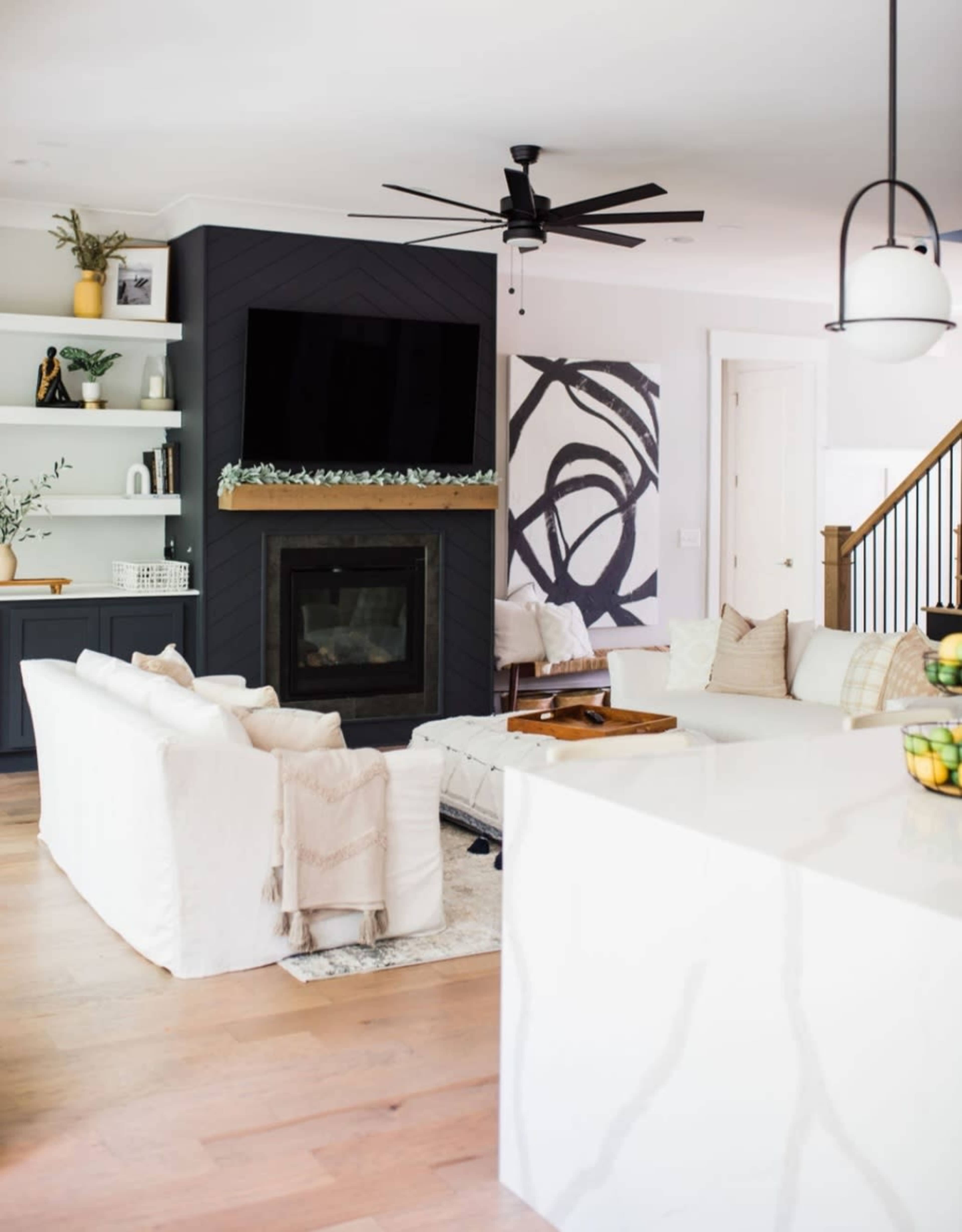 A modern living room features a fireplace with a dark accent wall, a large television mounted above it, and light-colored furniture arranged around a coffee table.
