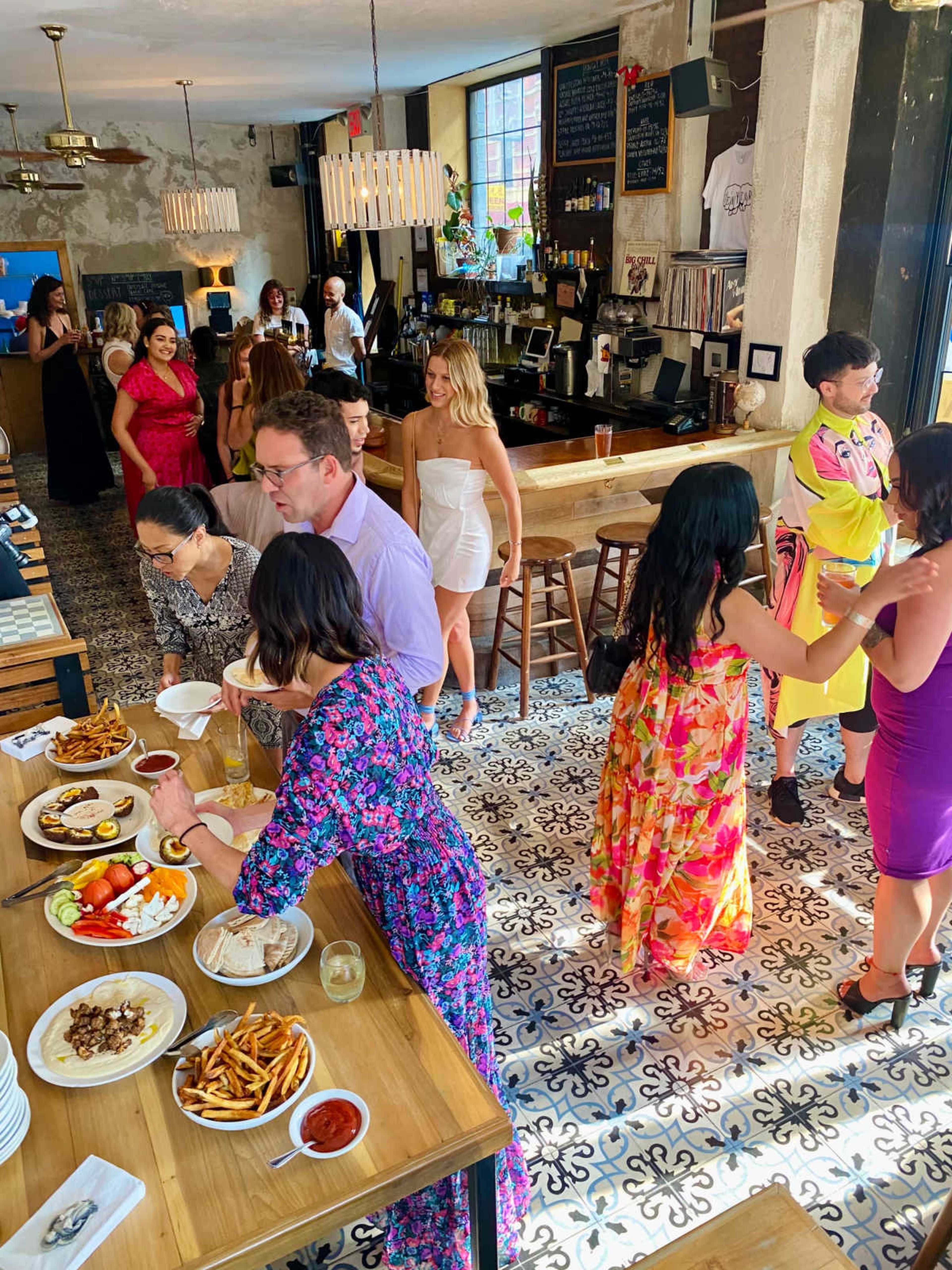 A lively restaurant scene features guests mingling, dining on various dishes, and enjoying drinks in an aesthetically designed space.