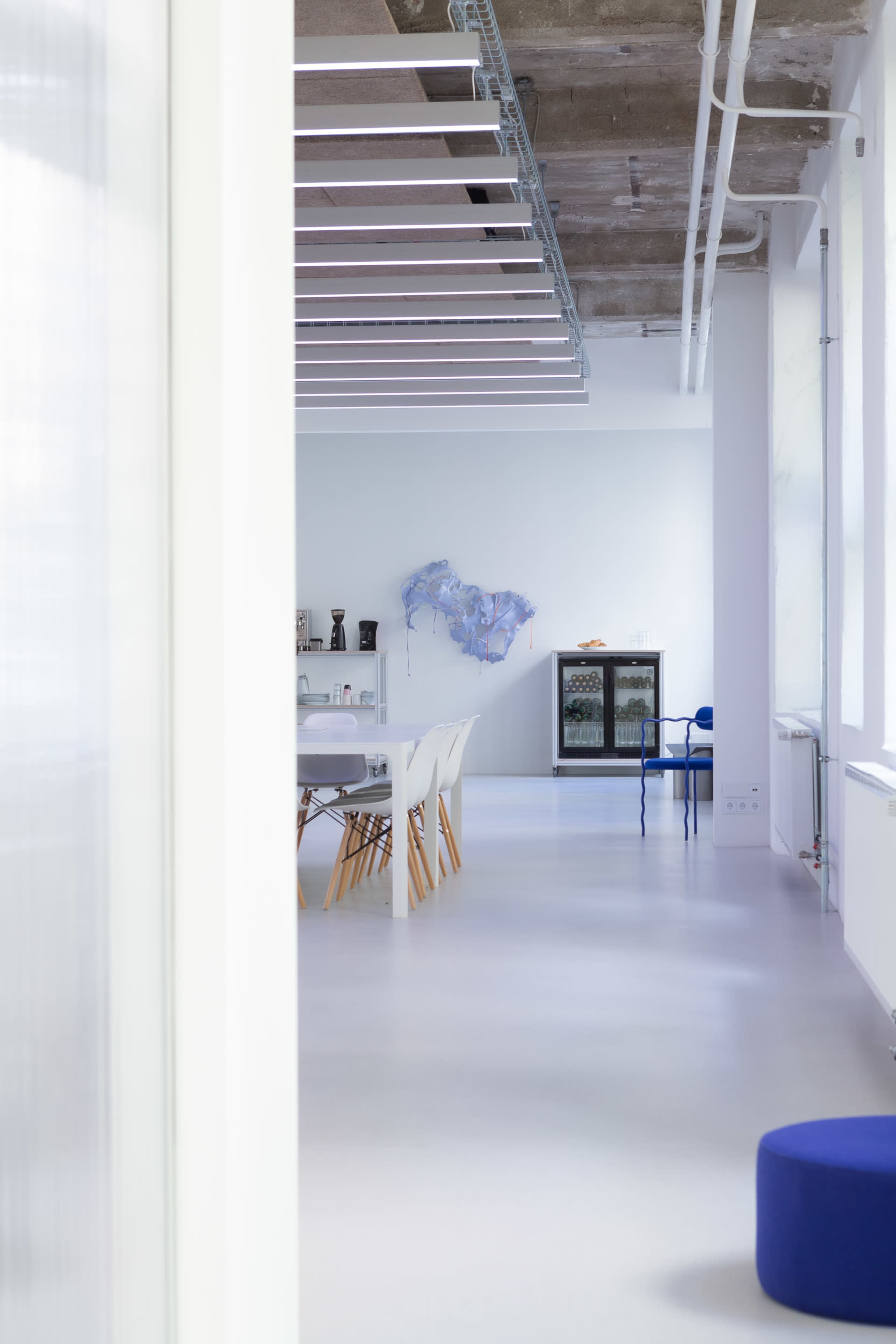 A modern, minimalistic interior space with a dining area, a decorative wall piece, and a blue cabinet.