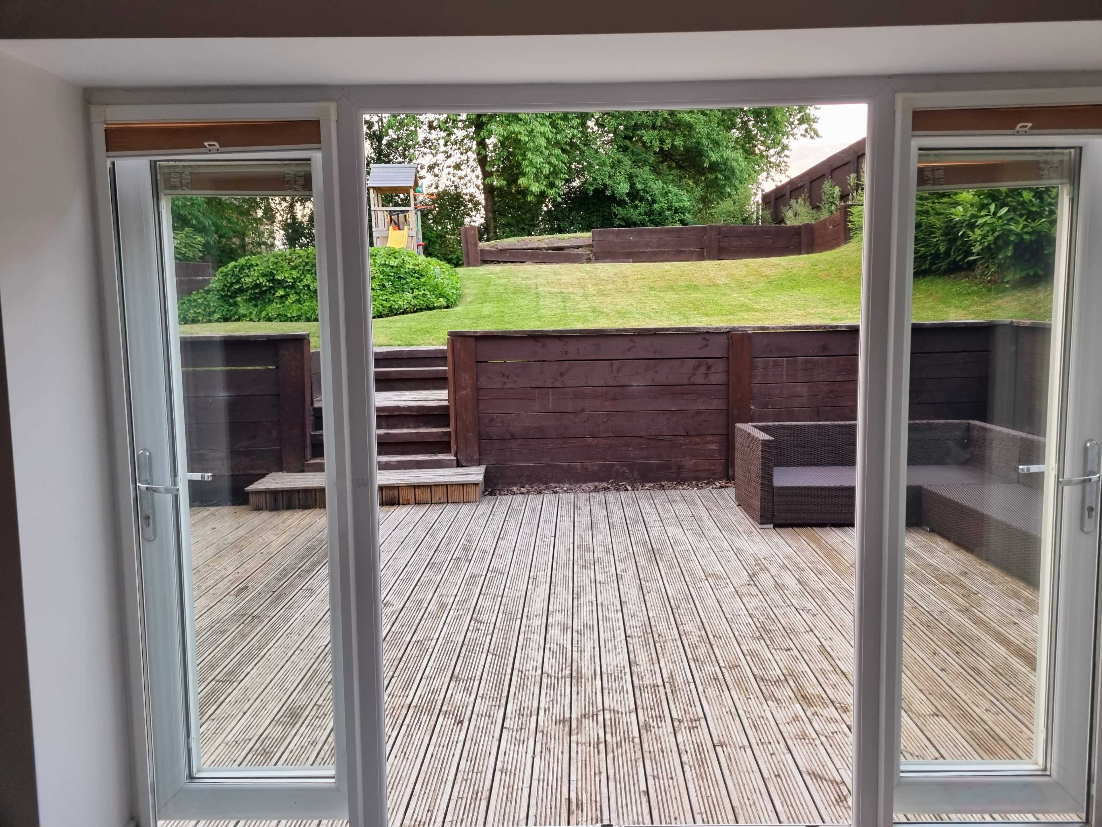 A wooden deck with sliding glass doors leading to a grassy backyard, featuring steps and seating furniture.