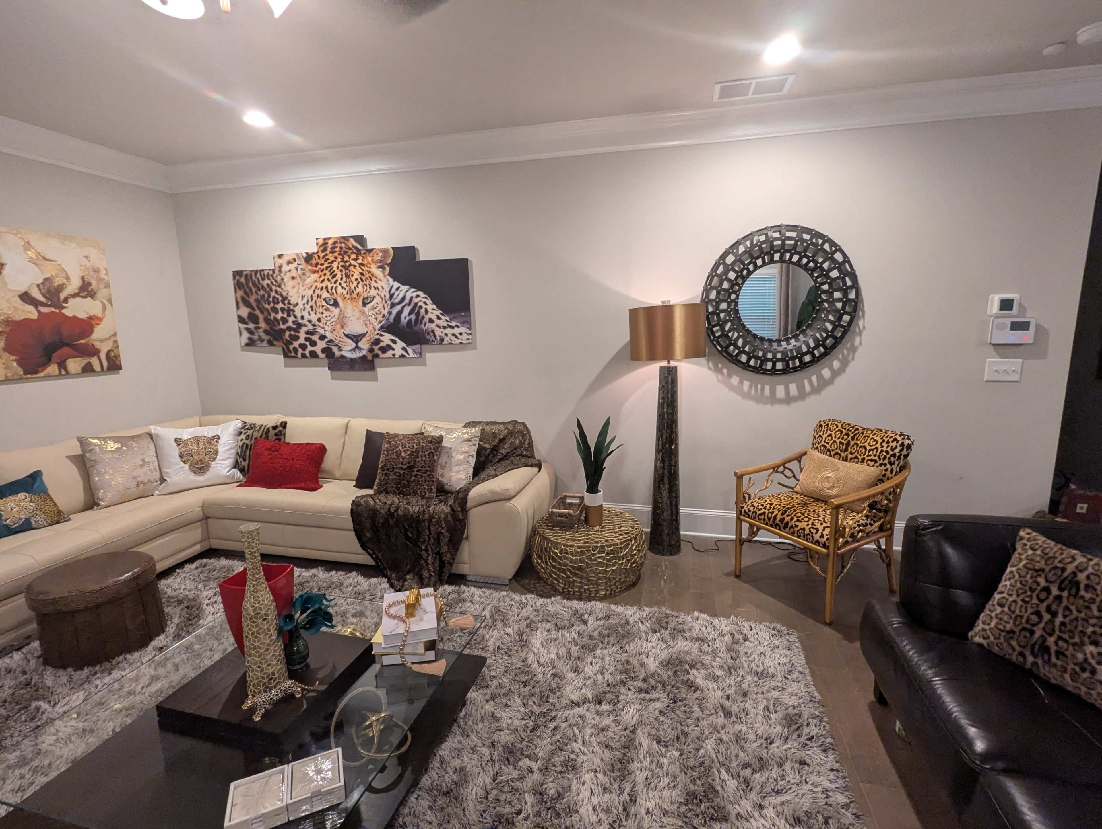 The living room features a cream-colored sectional sofa, a glass coffee table, and various decorative items, with a large leopard artwork on the wall and a chair upholstered in a leopard print.