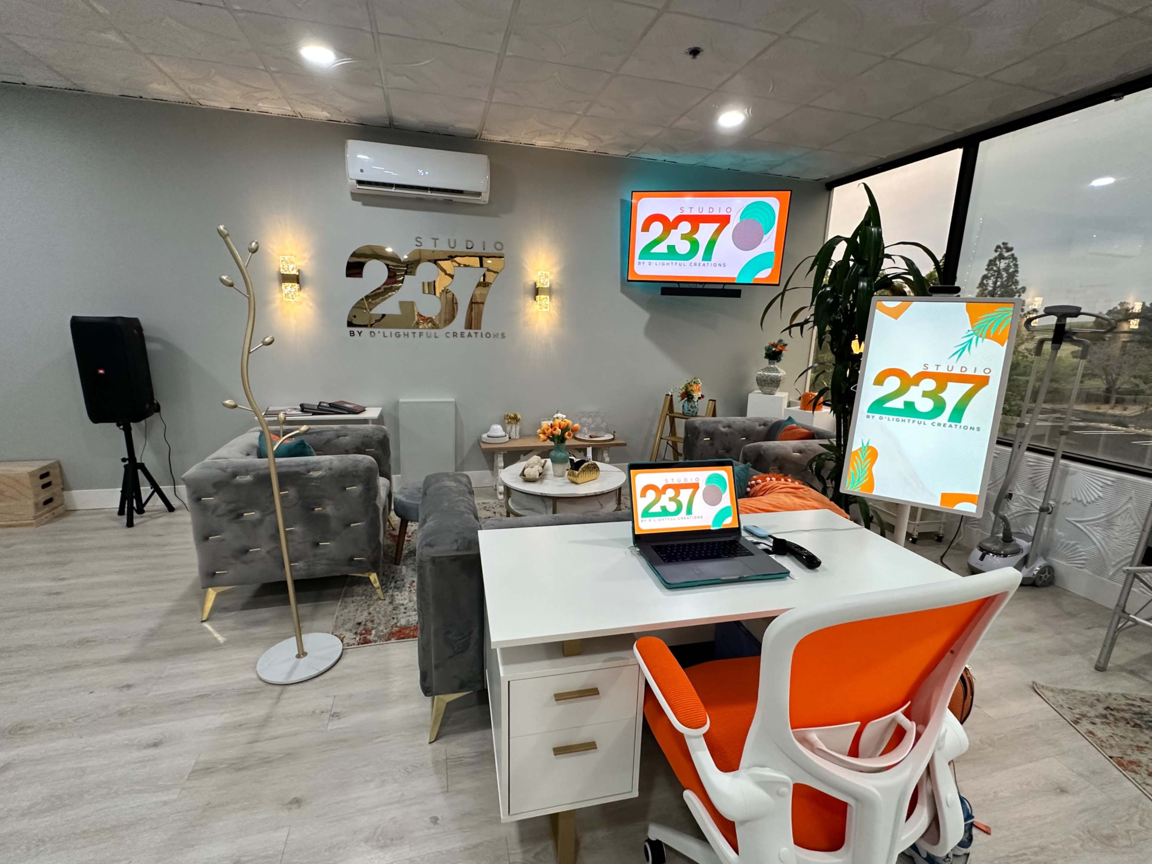 The image shows a modern office space with stylish furniture, a desk with a laptop, and two screens displaying the logo of Studio 257.