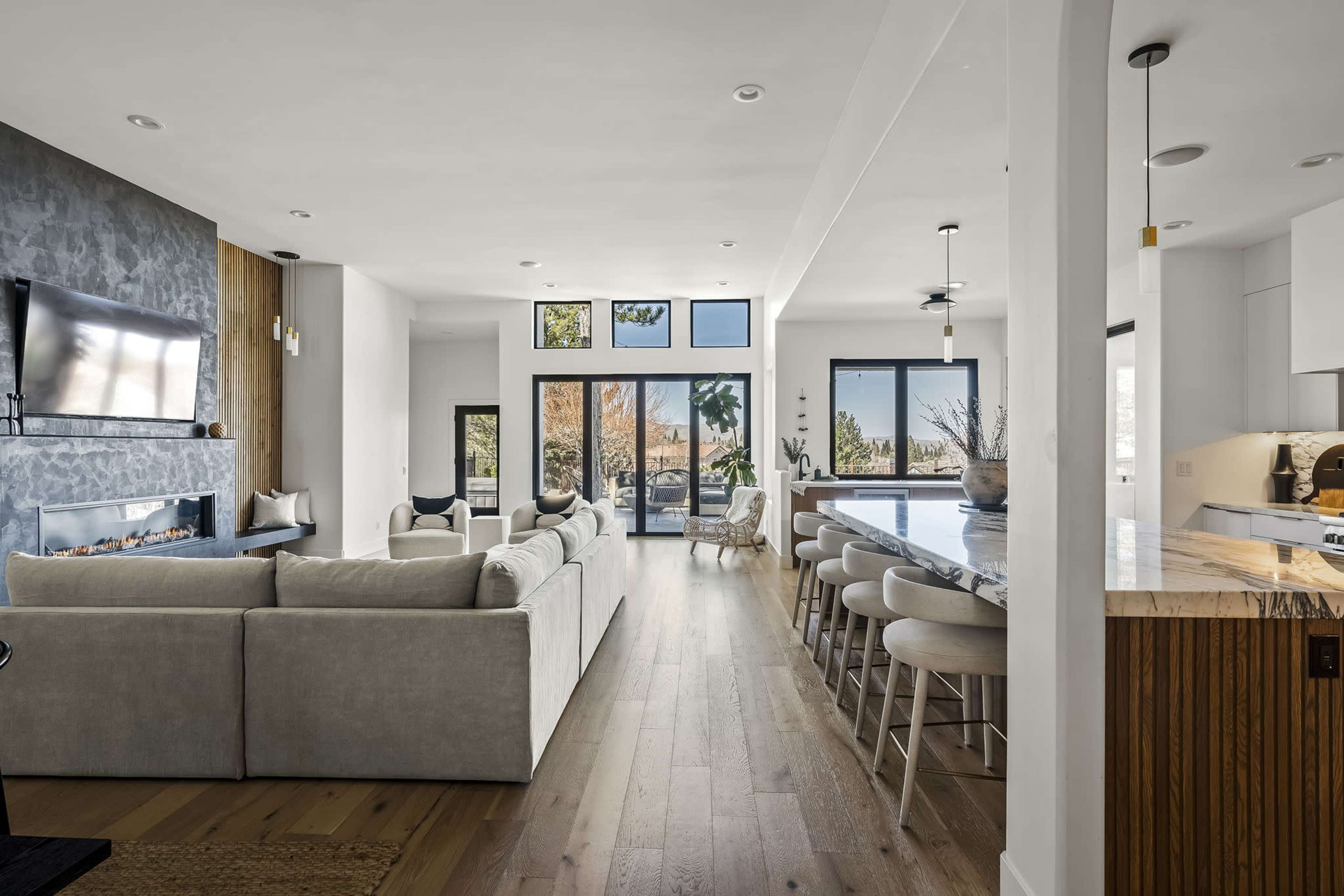 A modern living space featuring an open floor plan with a light-colored sectional sofa, a large kitchen island, and glass doors that lead to an outdoor area.