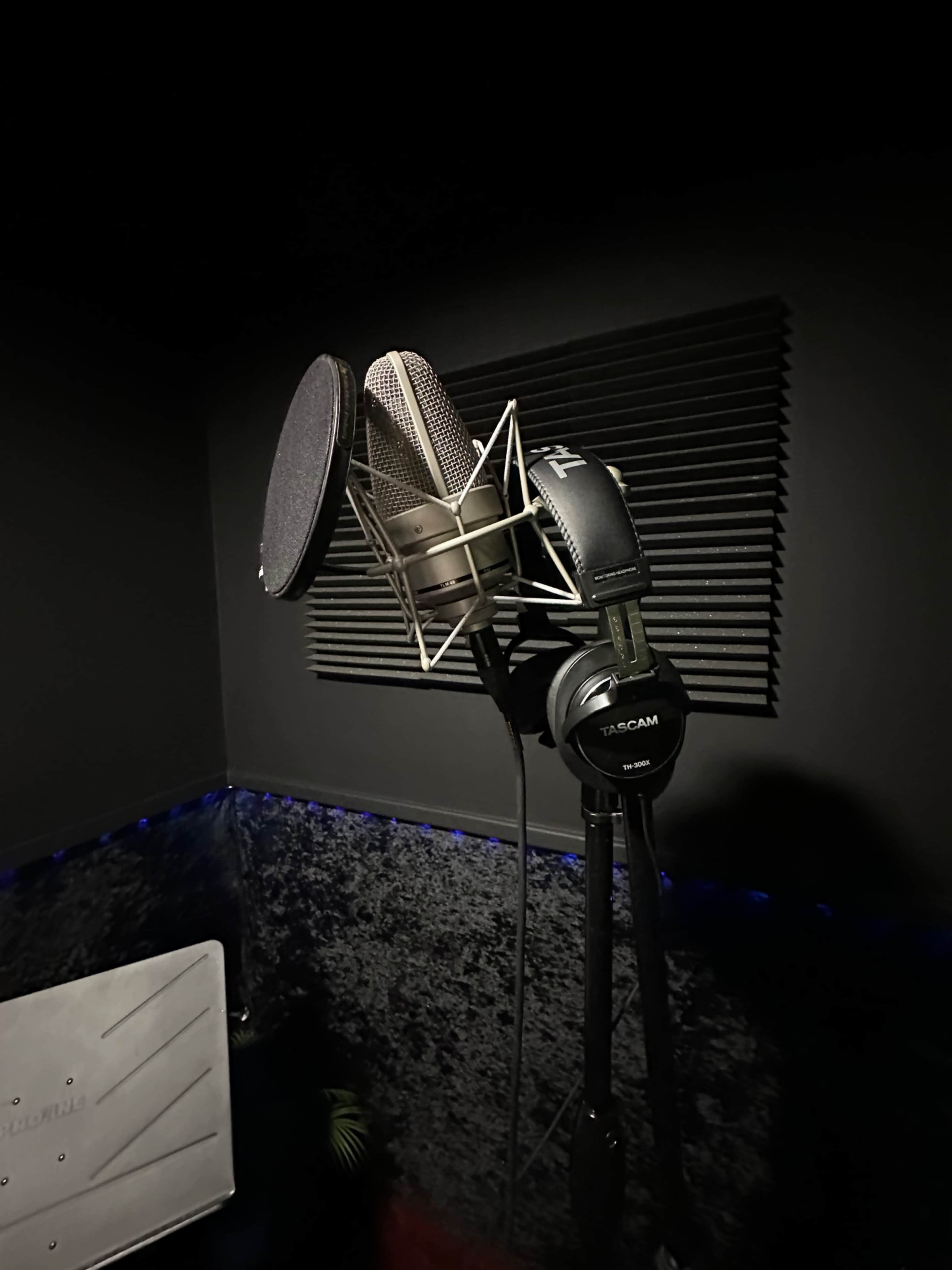 A microphone with pop filters and headphones is mounted in a soundproof recording booth.