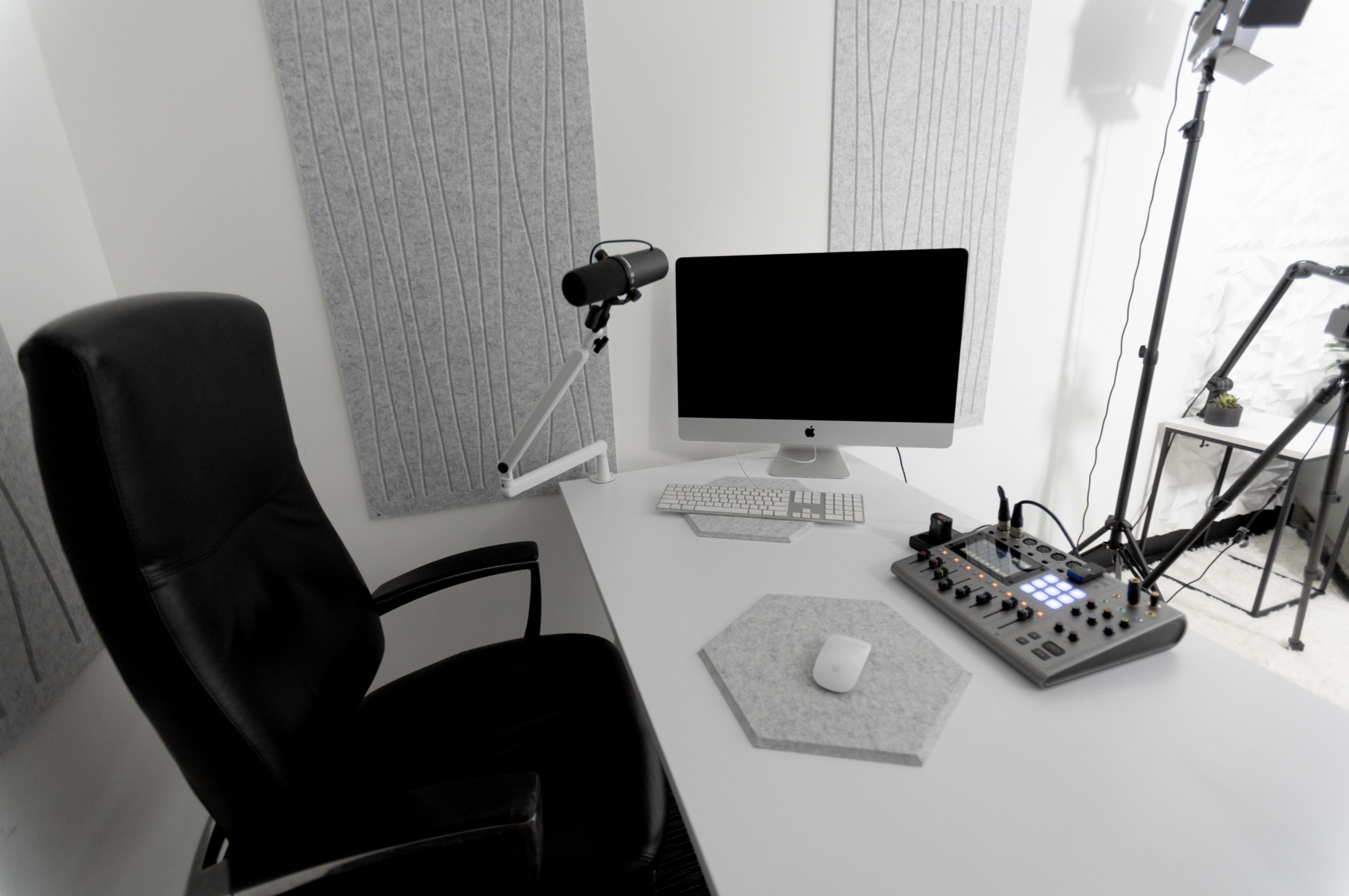 A modern workspace featuring a black office chair, an Apple computer on a white desk, and an audio mixer with various controls.