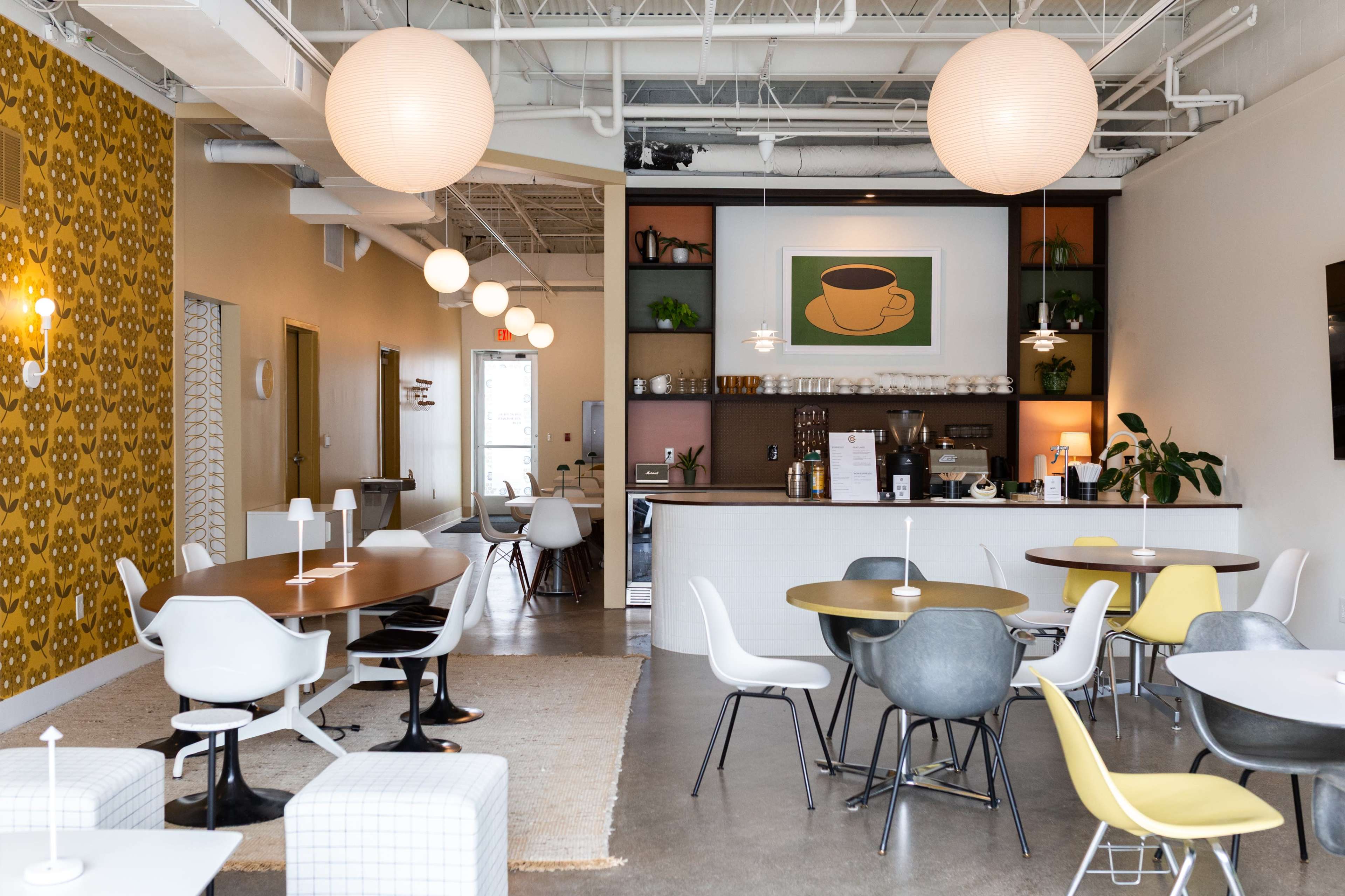 The image shows a modern café interior with various seating arrangements, a coffee station, and decorative wall art.