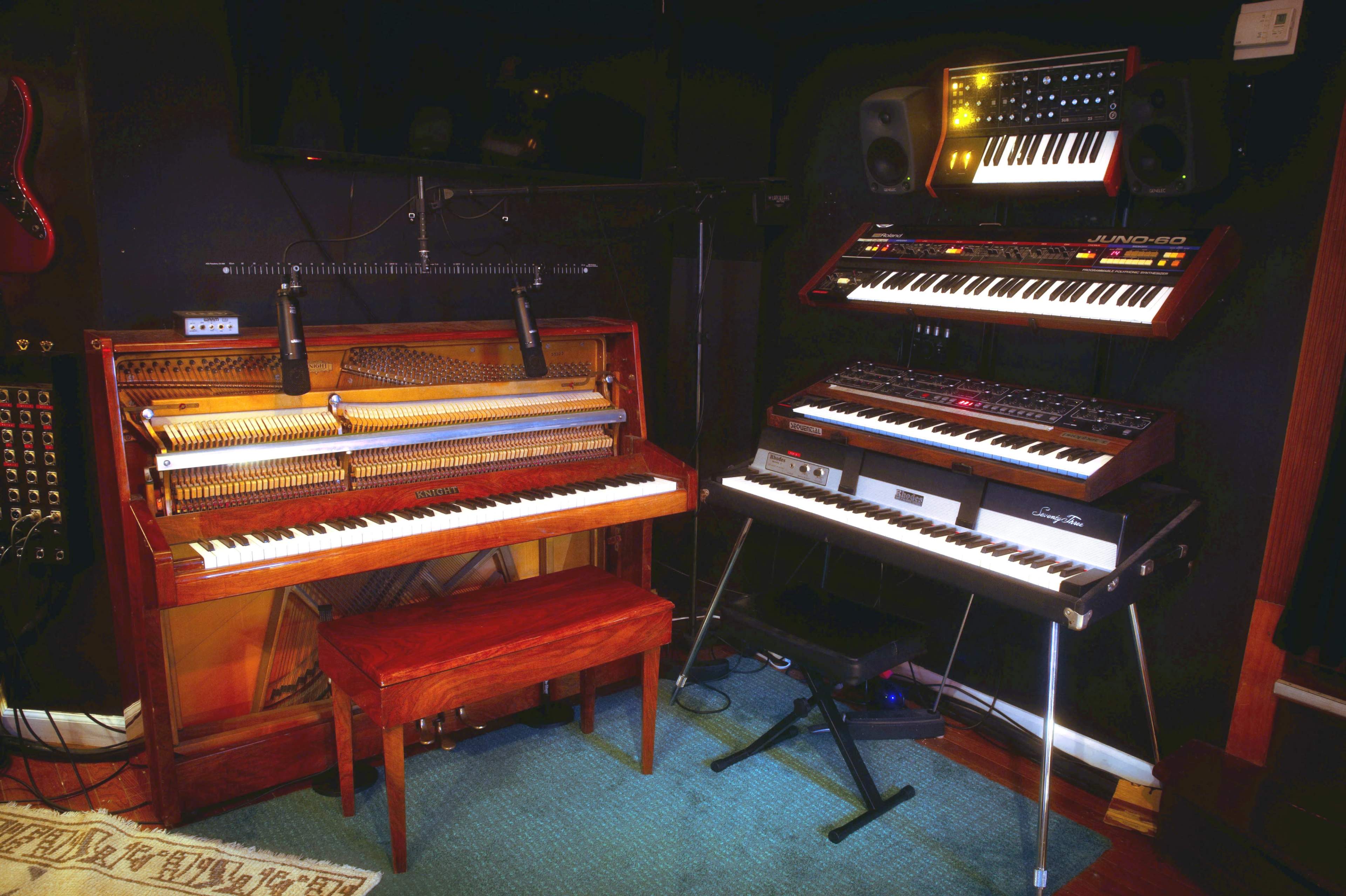 A music studio setup featuring a vintage piano on the left and two synthesizers on the right, with a mixing board above them.