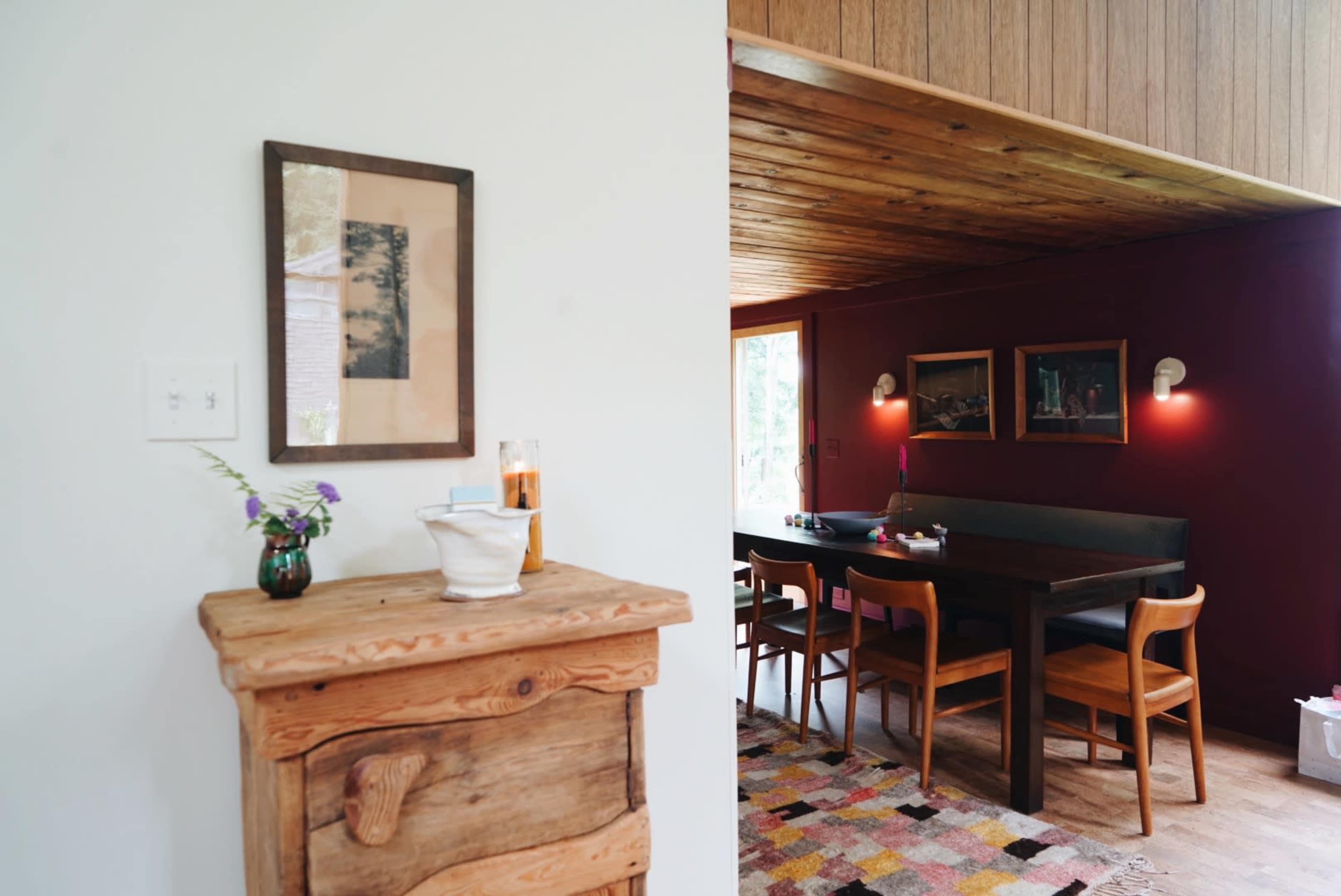 A cozy dining area features a wooden table surrounded by chairs, with framed artwork on the walls and a small vase of flowers on a side table.