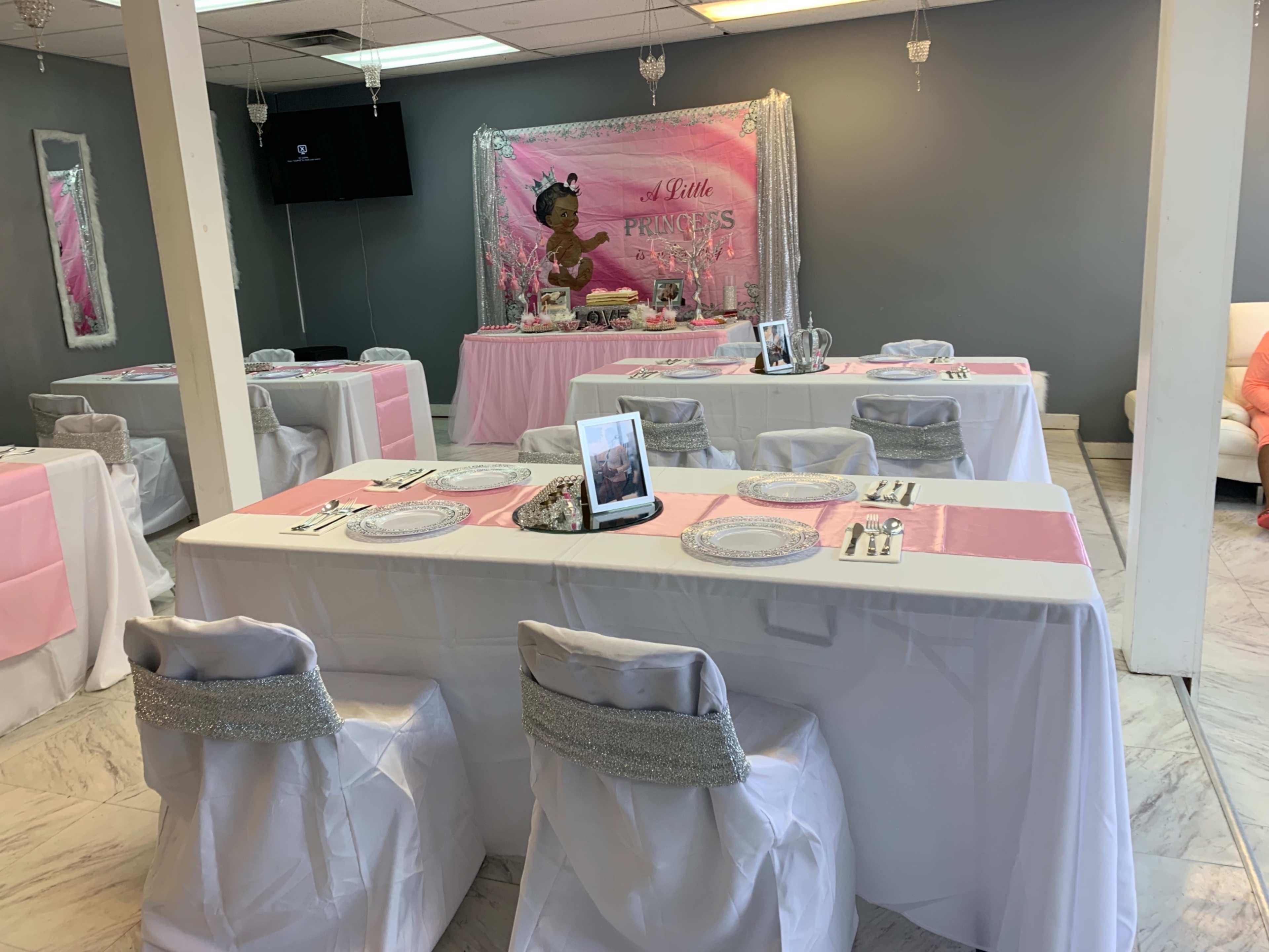 An elegantly arranged party space with white tables covered in pink runners, decorative chairs, and a themed backdrop featuring a character.