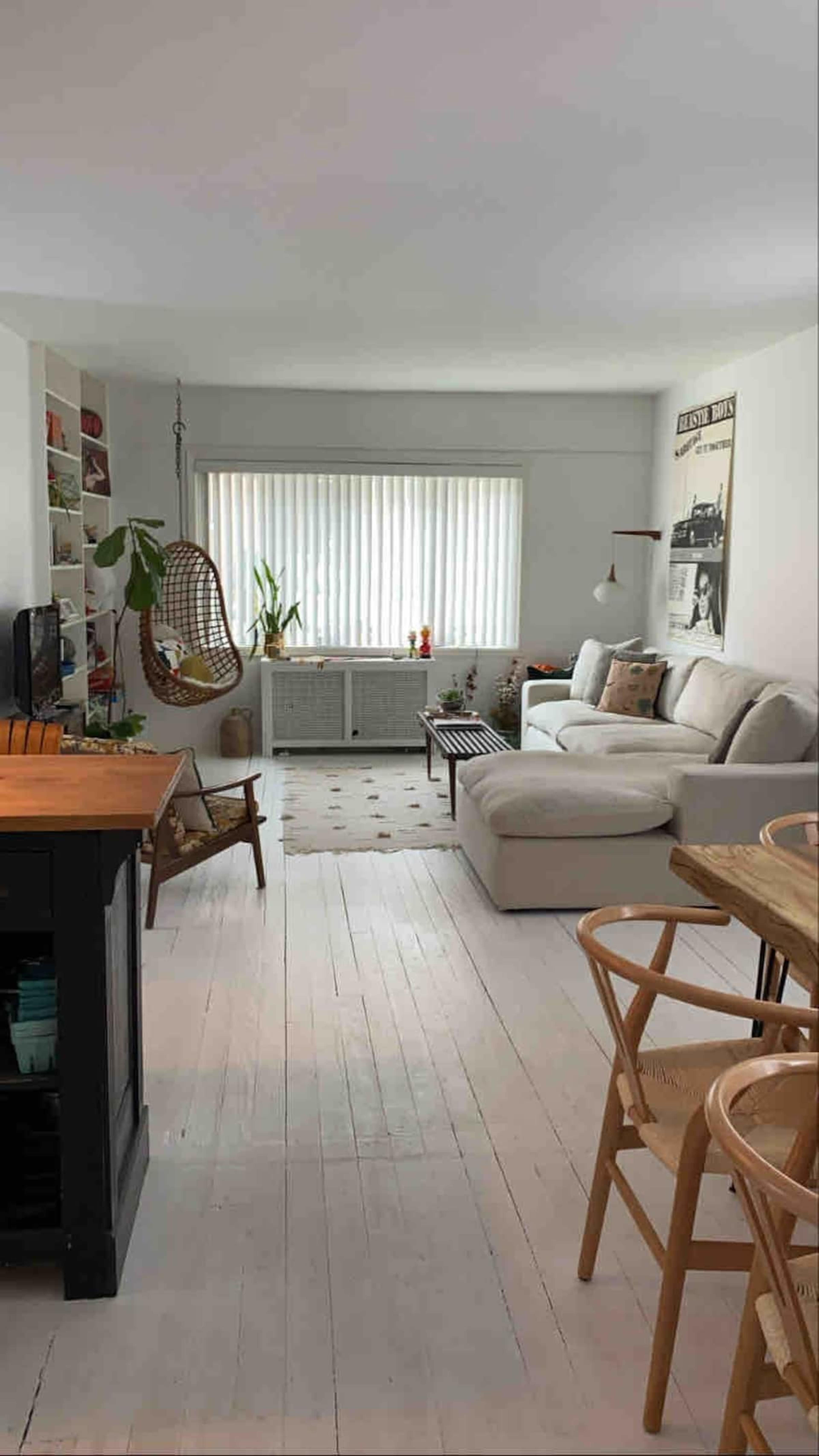 A bright, open living space featuring a white sofa, a hanging chair, and a wooden dining table surrounded by chairs.