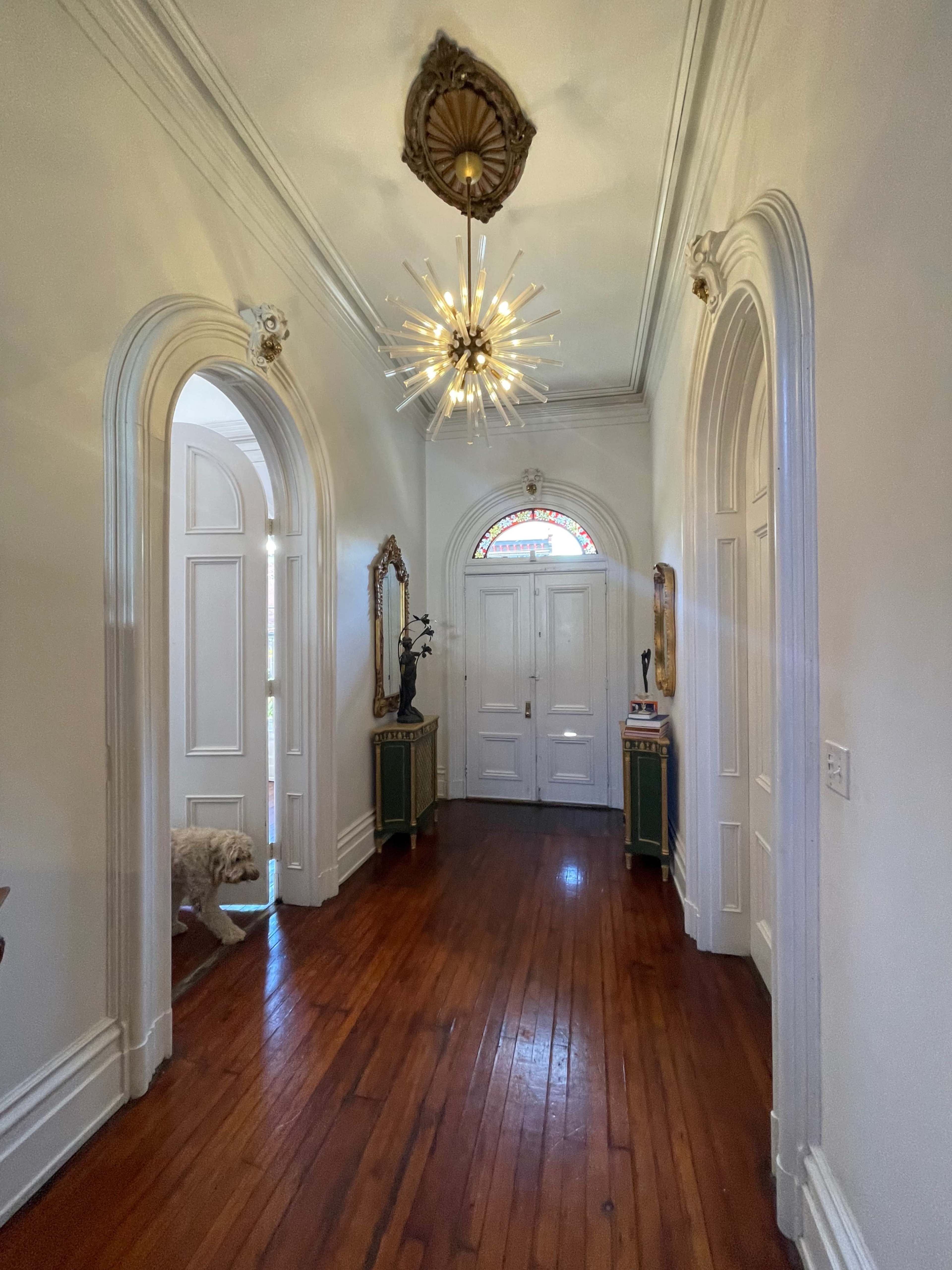 A long hallway features arched doorways, a decorative chandelier, wooden flooring, and various ornate decorations along the walls.