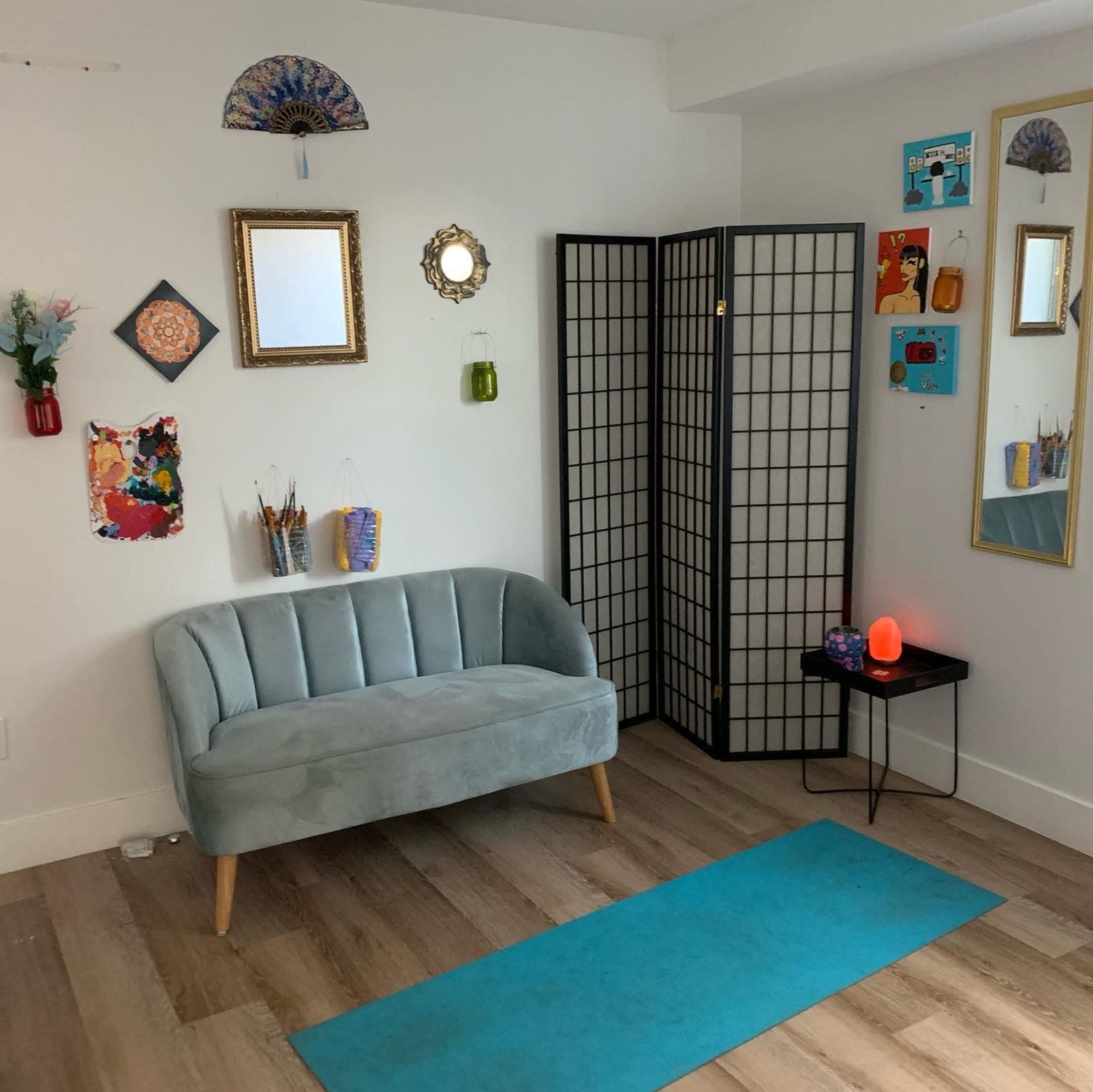 A cozy sitting area features a light blue sofa, a decorative folding screen, and various artworks on the walls.