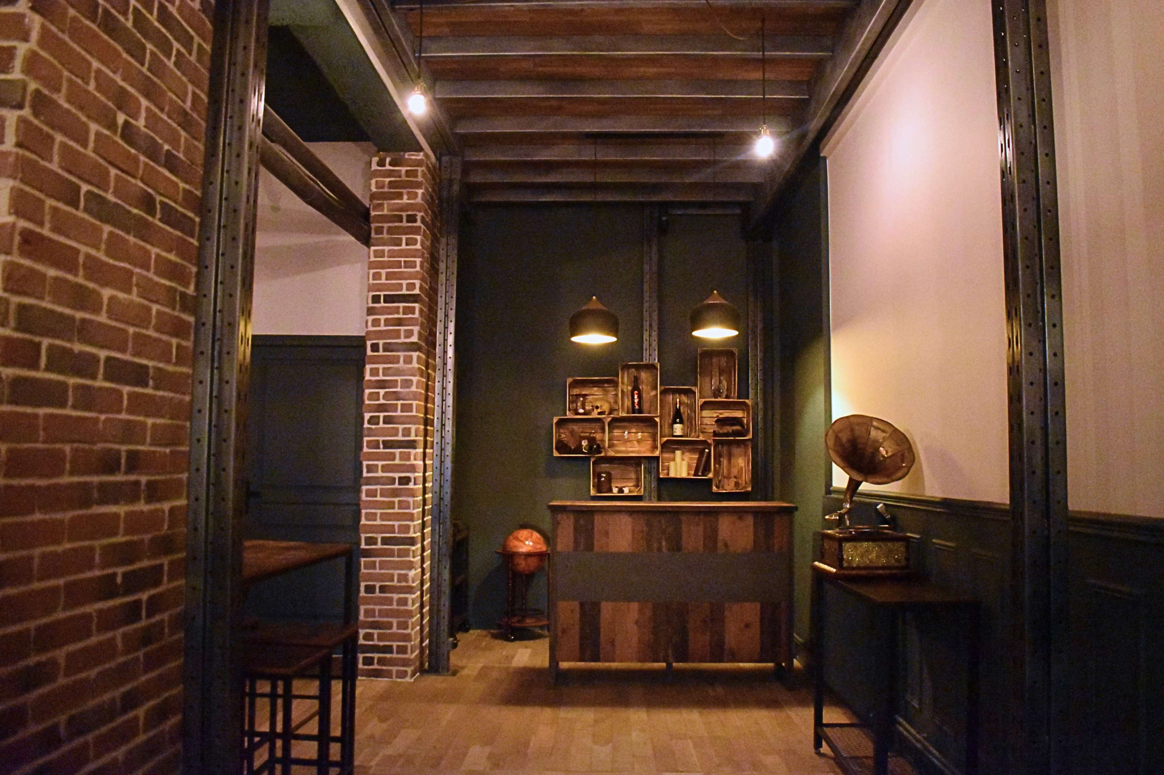 An interior space featuring a wooden reception desk against a dark green wall, with decorative shelves and vintage objects, including an antique gramophone.