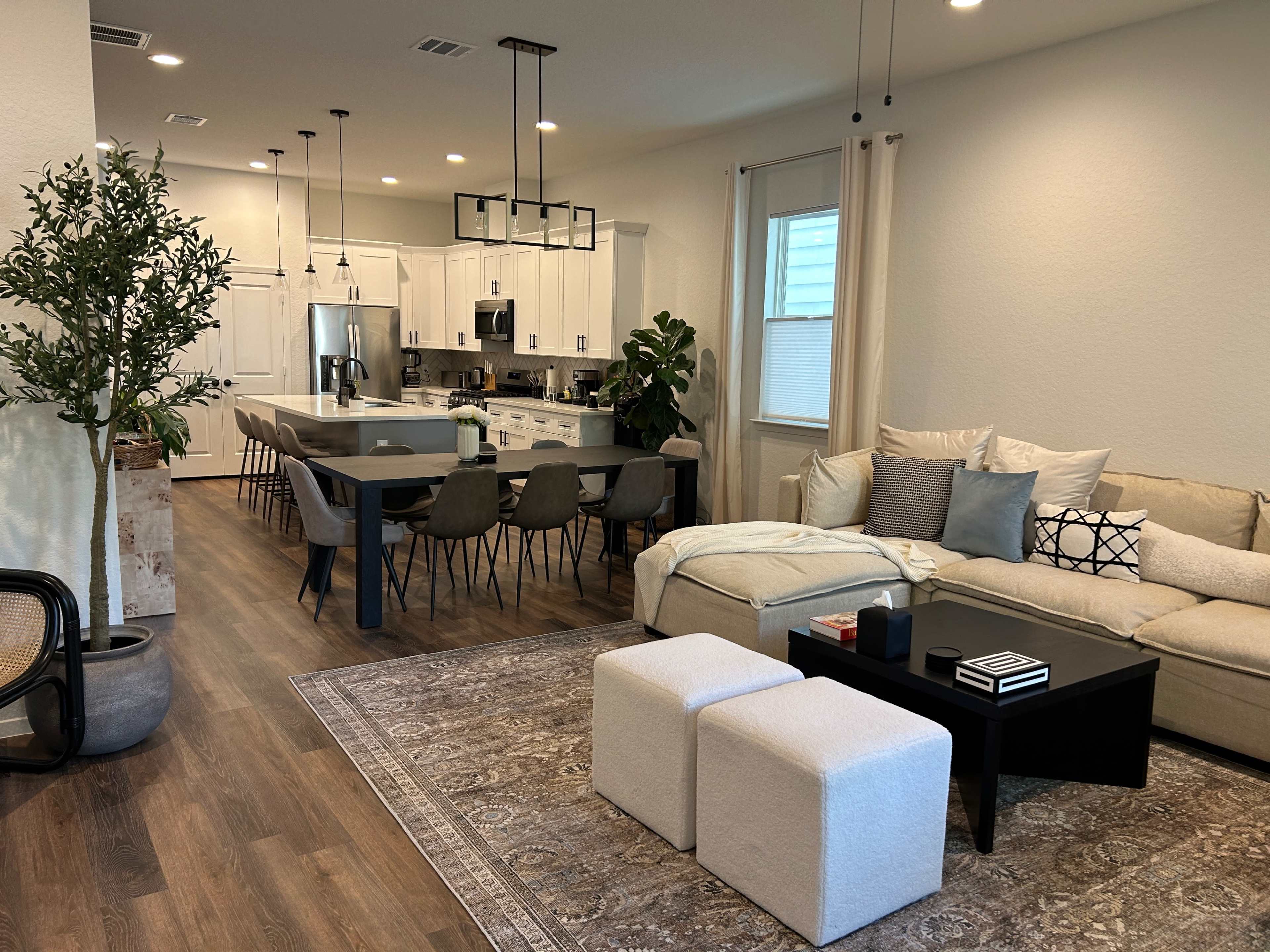 A modern living space featuring an open-concept layout with a sofa, coffee table, dining table, and a kitchen in the background.