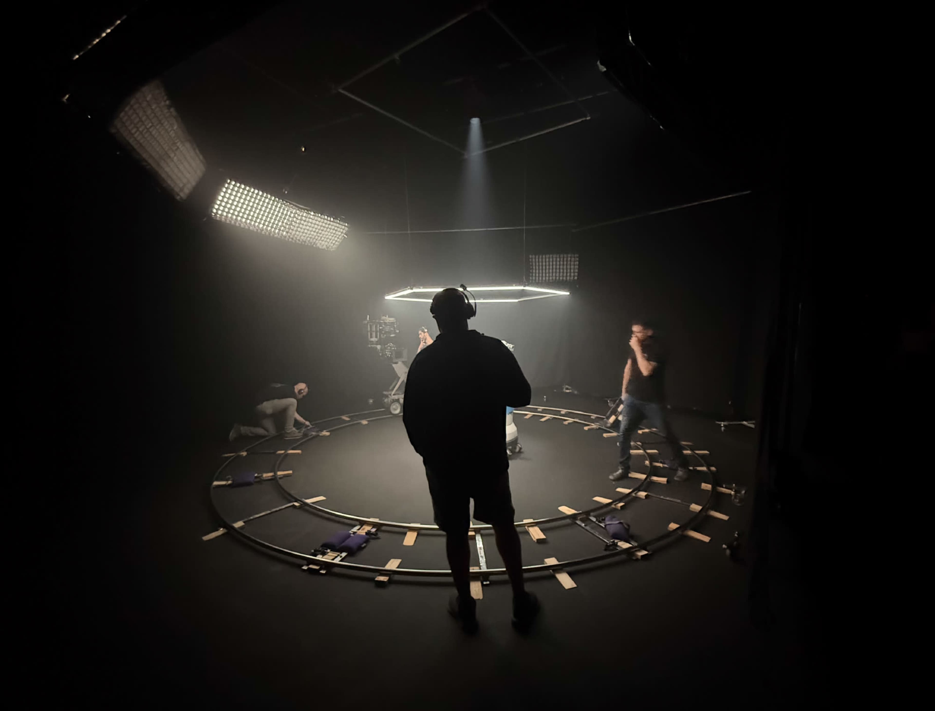 A crew prepares equipment in a dimly lit studio with a circular track and overhead lighting.