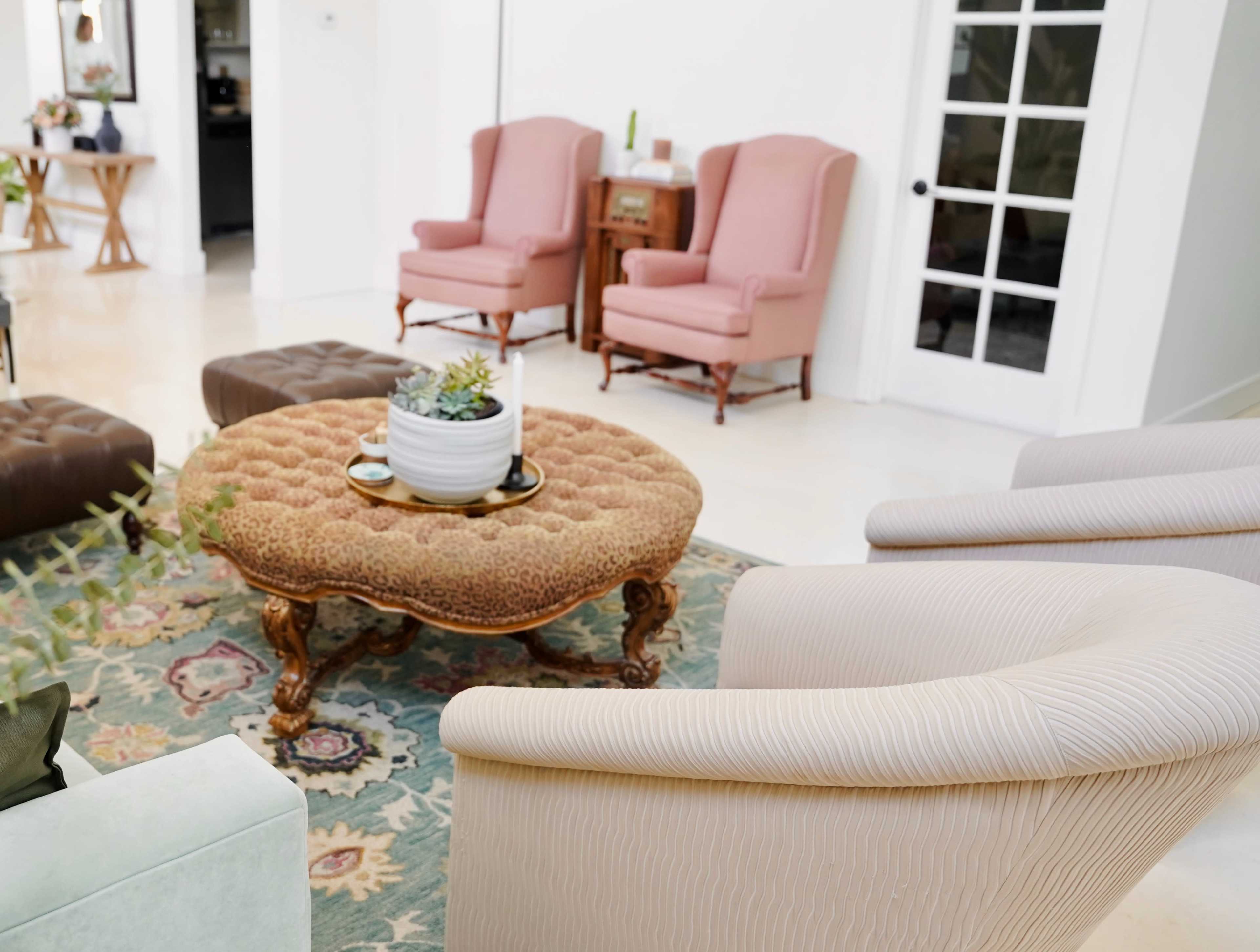 A spacious living area with two pink wingback chairs, a round coffee table with a plant, and a patterned area rug.