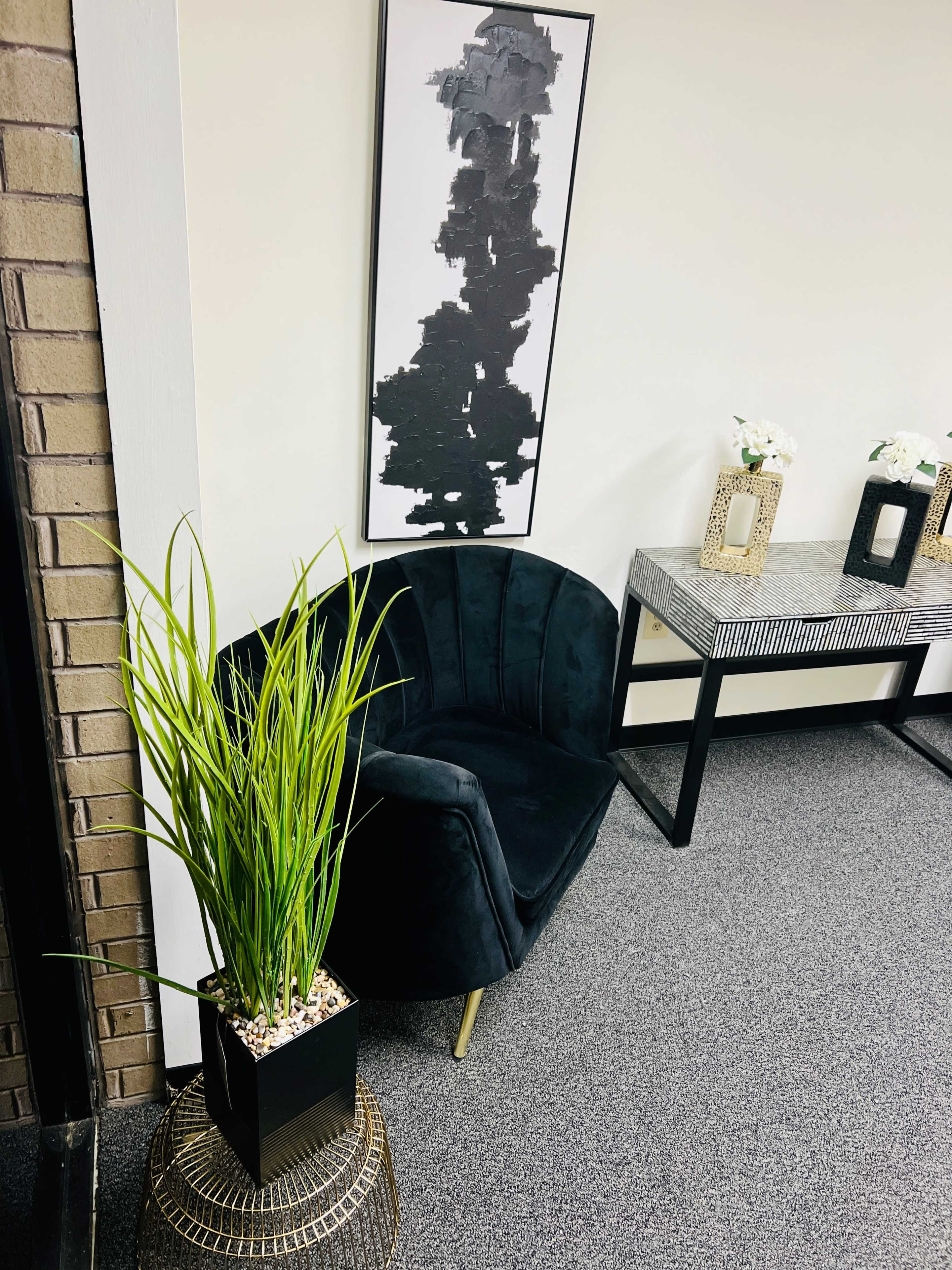 The scene features a black velvet chair beside a geometric side table, with a large abstract painting on the wall and decorative plants in a modern pot.