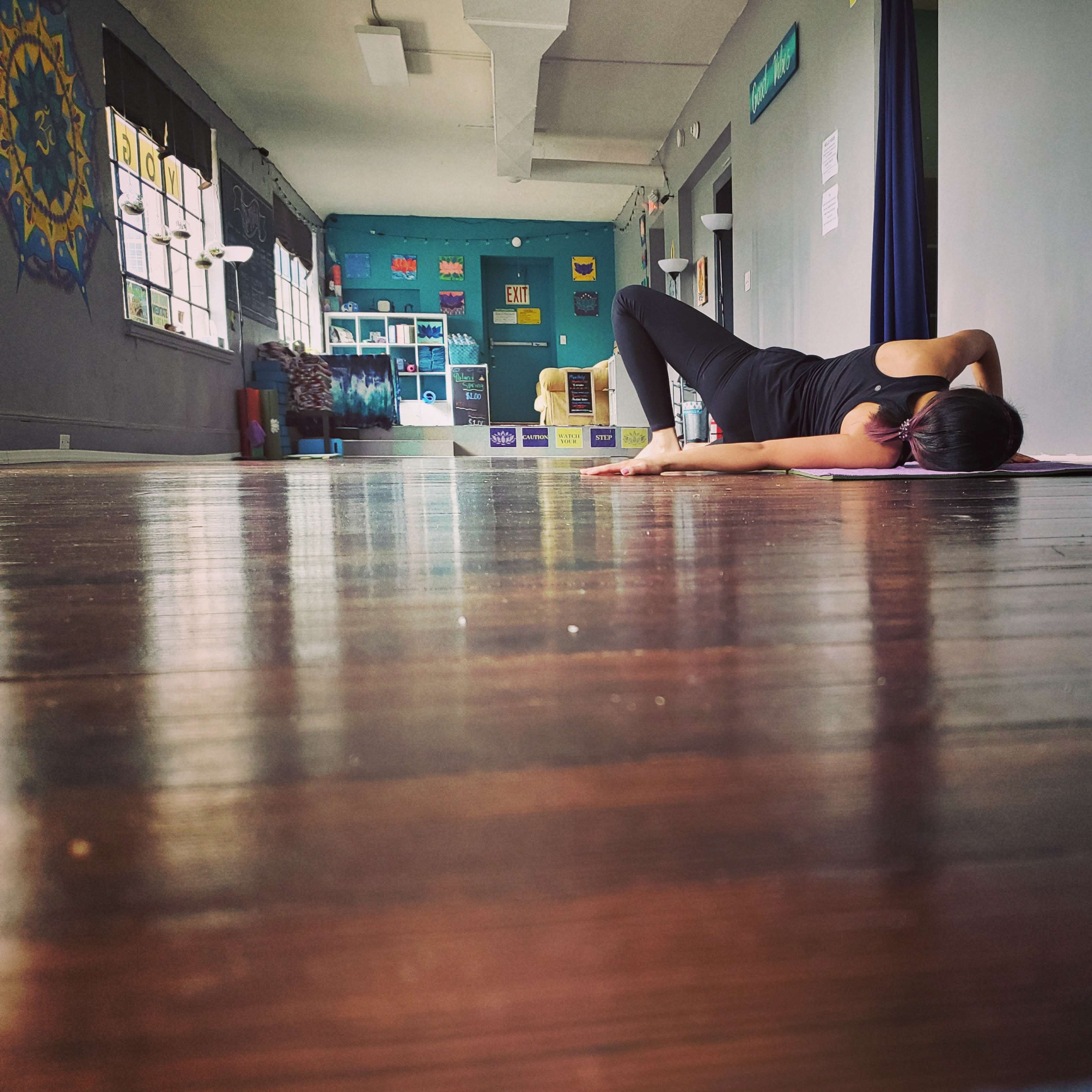 A person lies on a yoga mat on a polished wooden floor in a brightly colored studio.