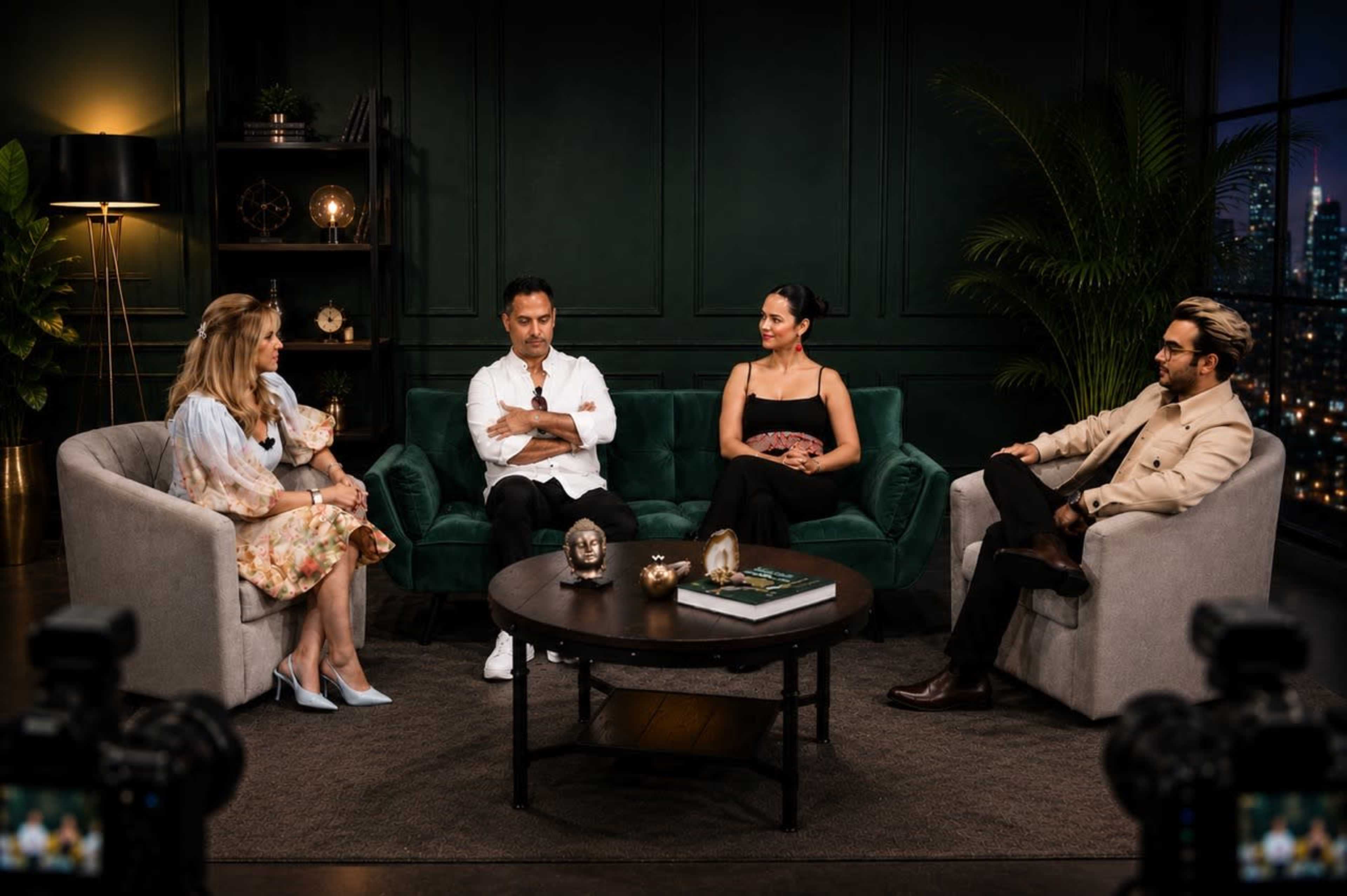 A group of four people sits in a well-lit room with green walls, on modern sofas arranged around a coffee table.