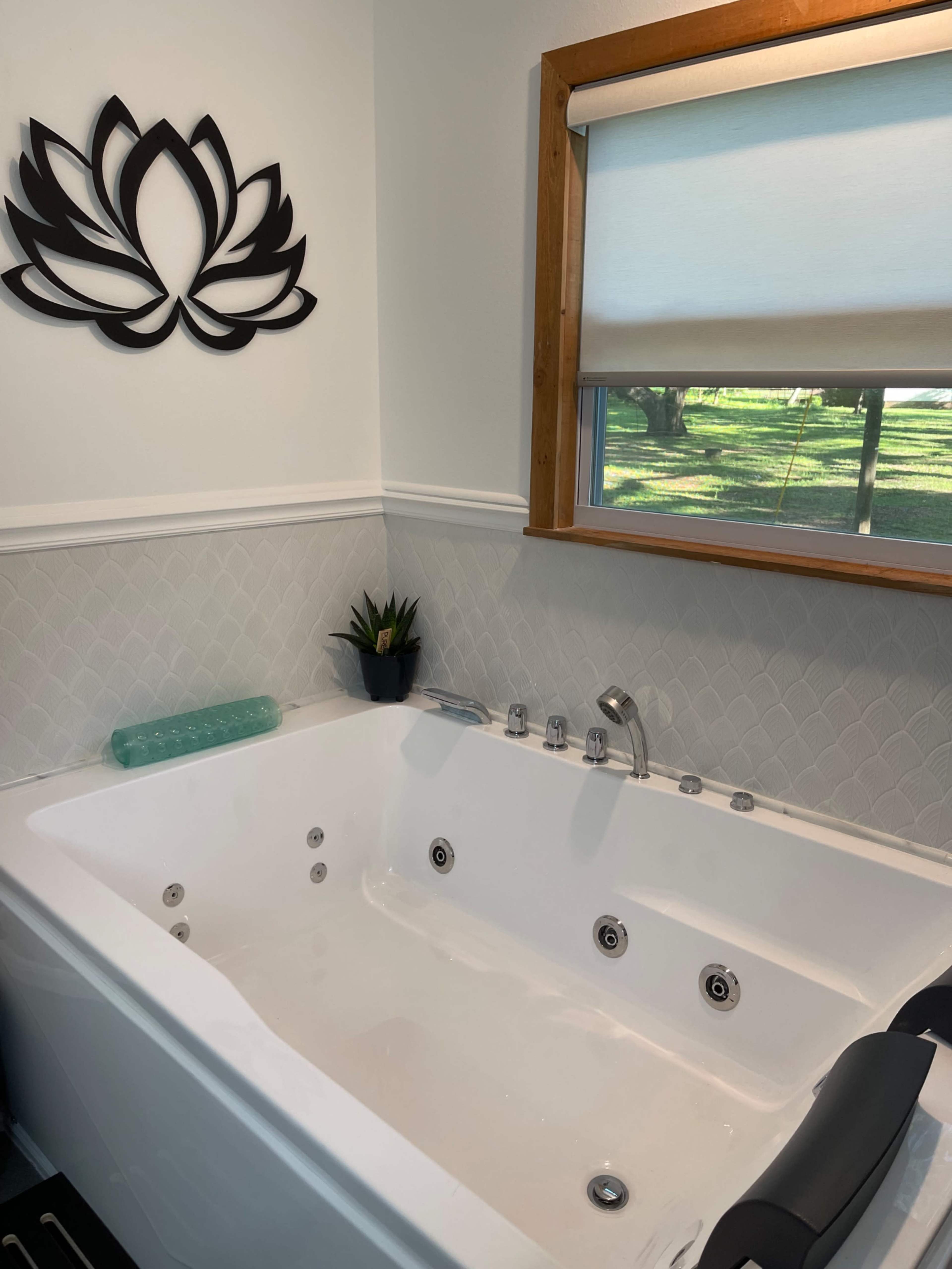 The image shows a modern Jacuzzi bathtub situated against a wall with a window and a decorative lotus flower above it.