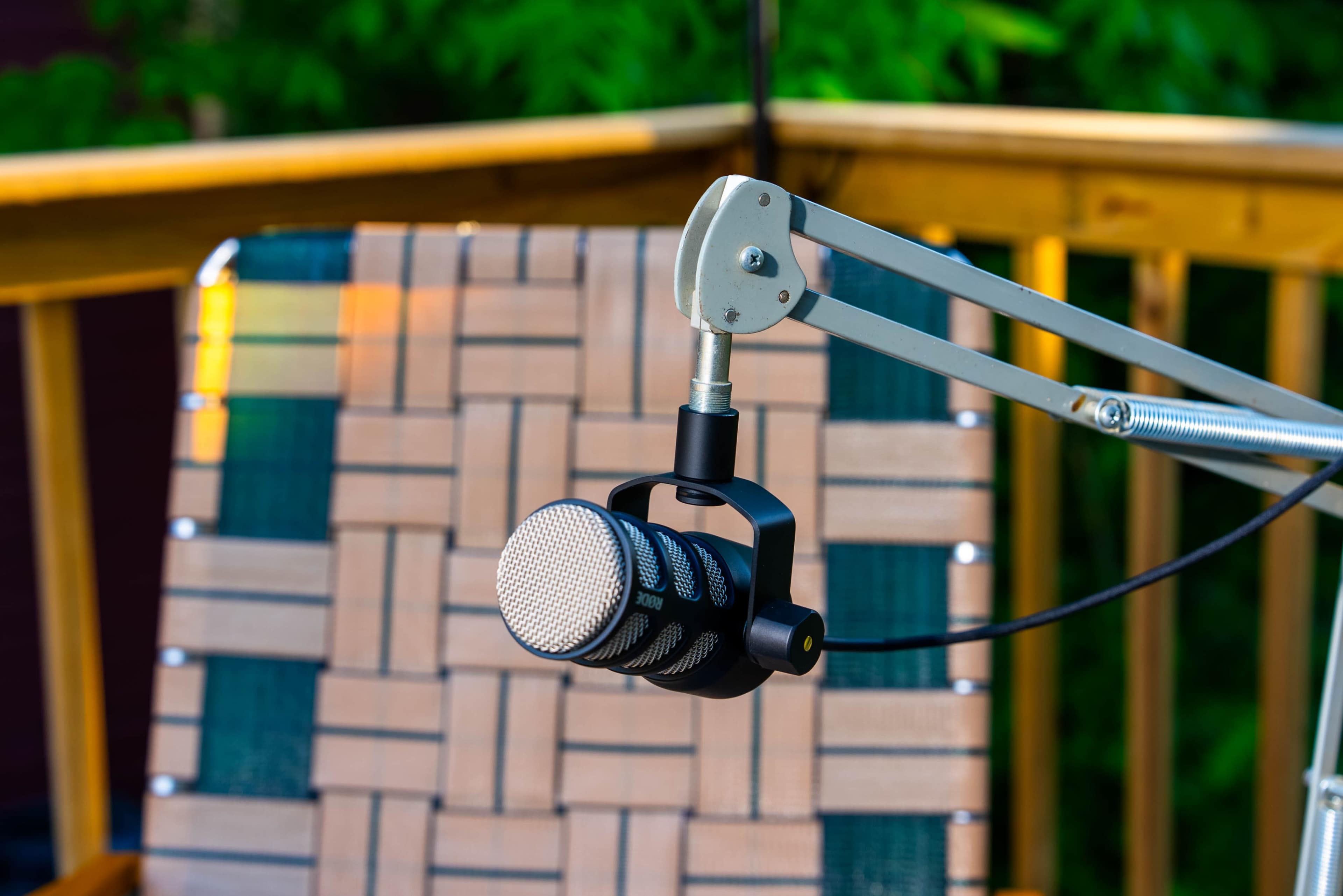 A microphone is suspended from an adjustable arm above a woven chair on a deck.