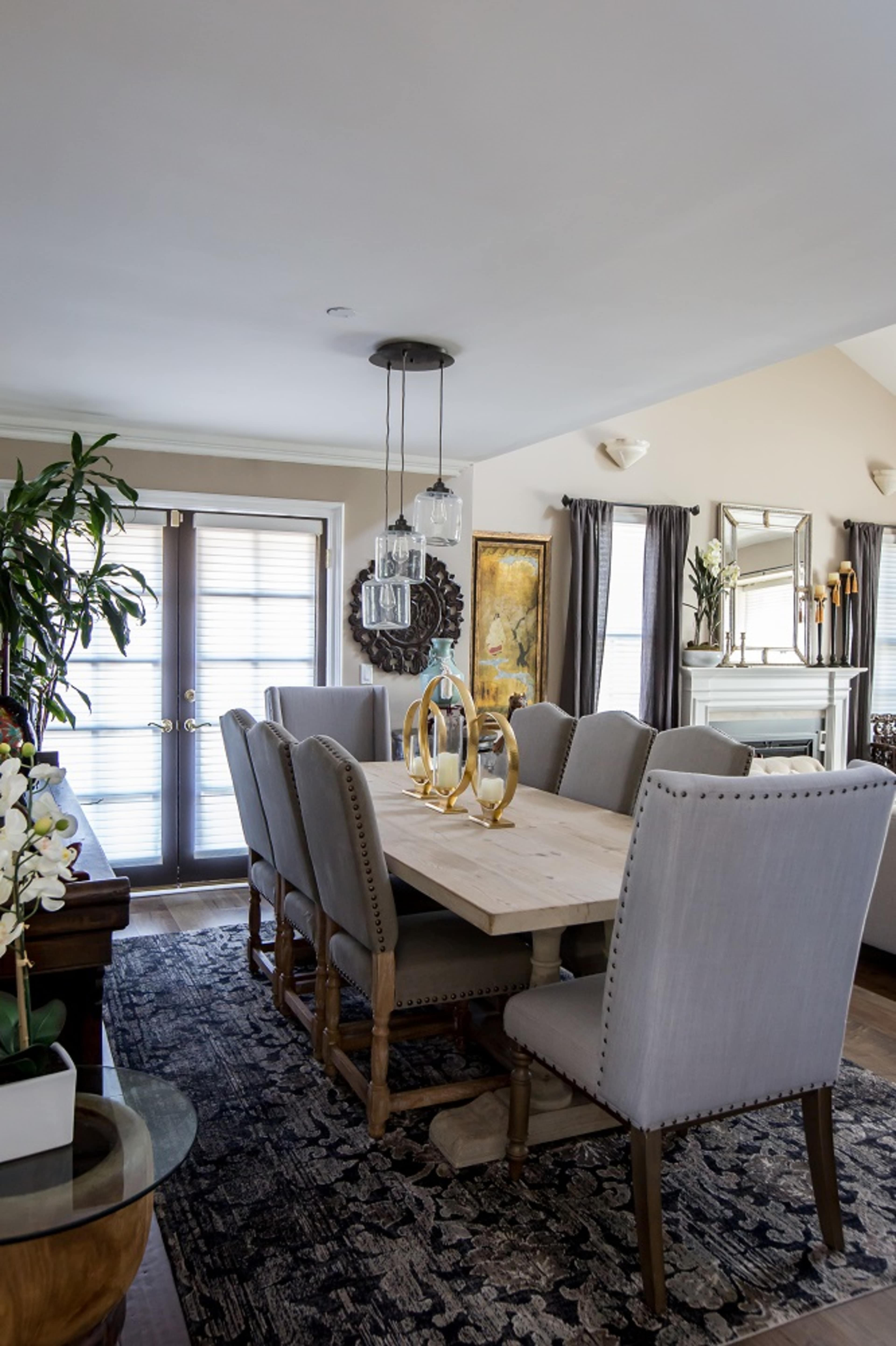 A dining room features a wooden table surrounded by upholstered chairs, with a sliding glass door and decorative elements in the background.