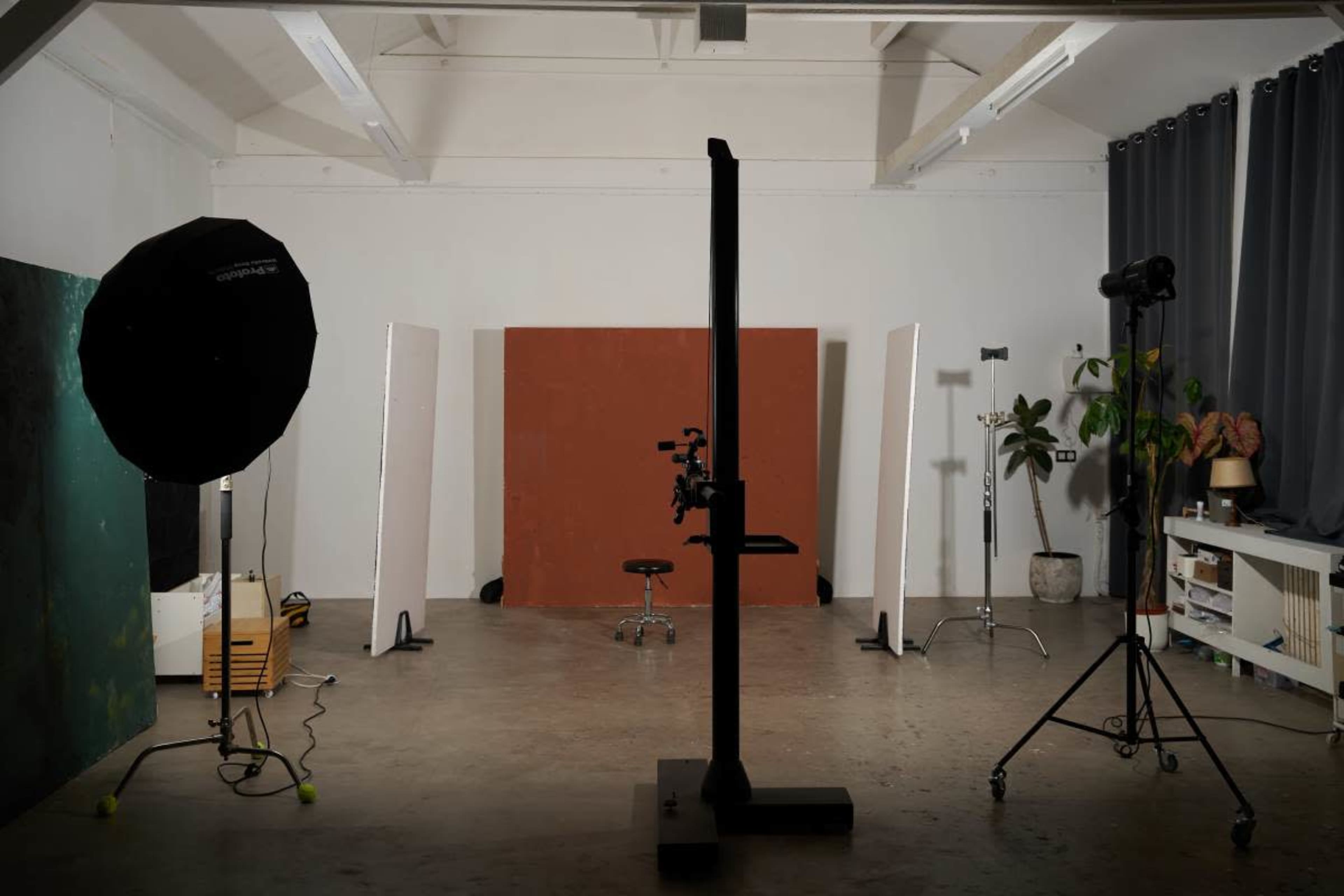 The image shows a photography studio with a backdrop, lighting equipment, and a stool arranged in the space.