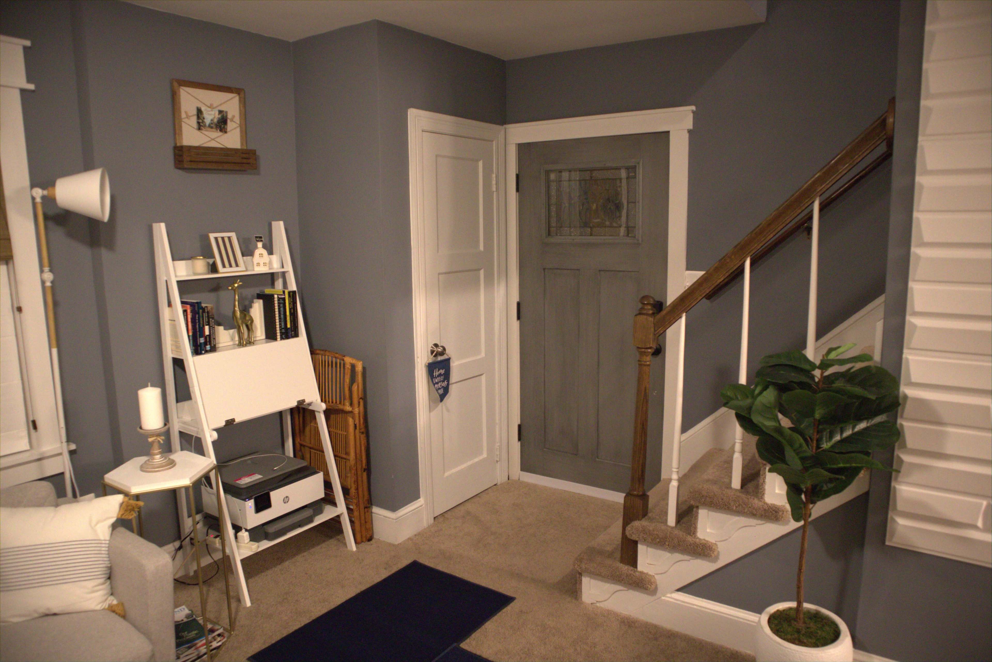 A cozy corner of a room with a gray wall, a door with a glass panel, a staircase, a small bookshelf, and a plant in a pot.