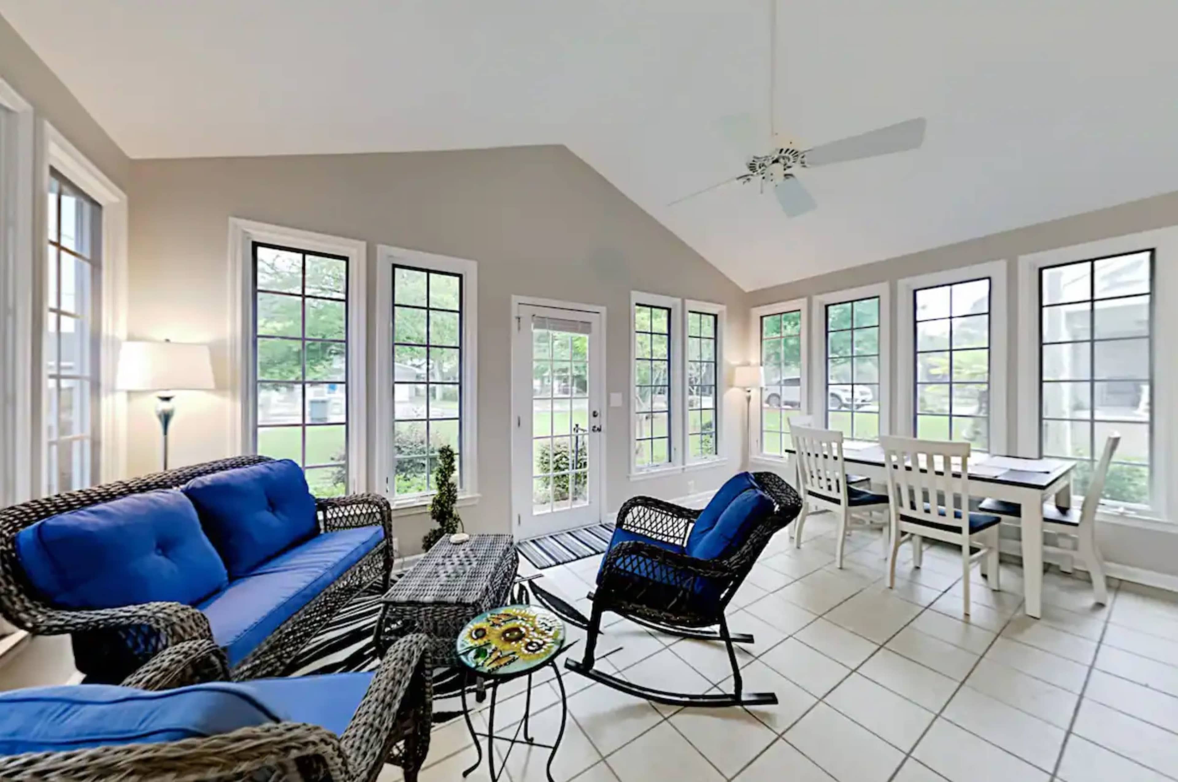 The sunroom features blue upholstered seating, a dining area, and large windows that provide natural light.