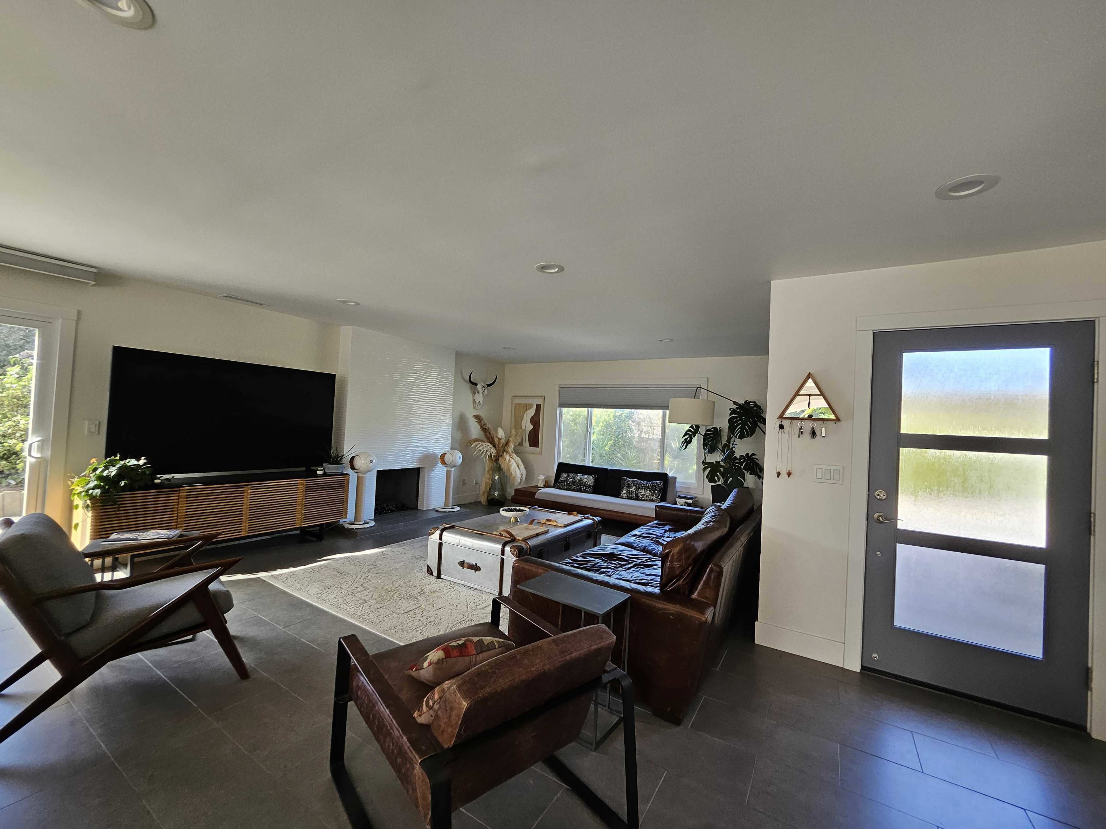 A modern living room with a large television, a sectional sofa, a coffee table, and a door leading outside.